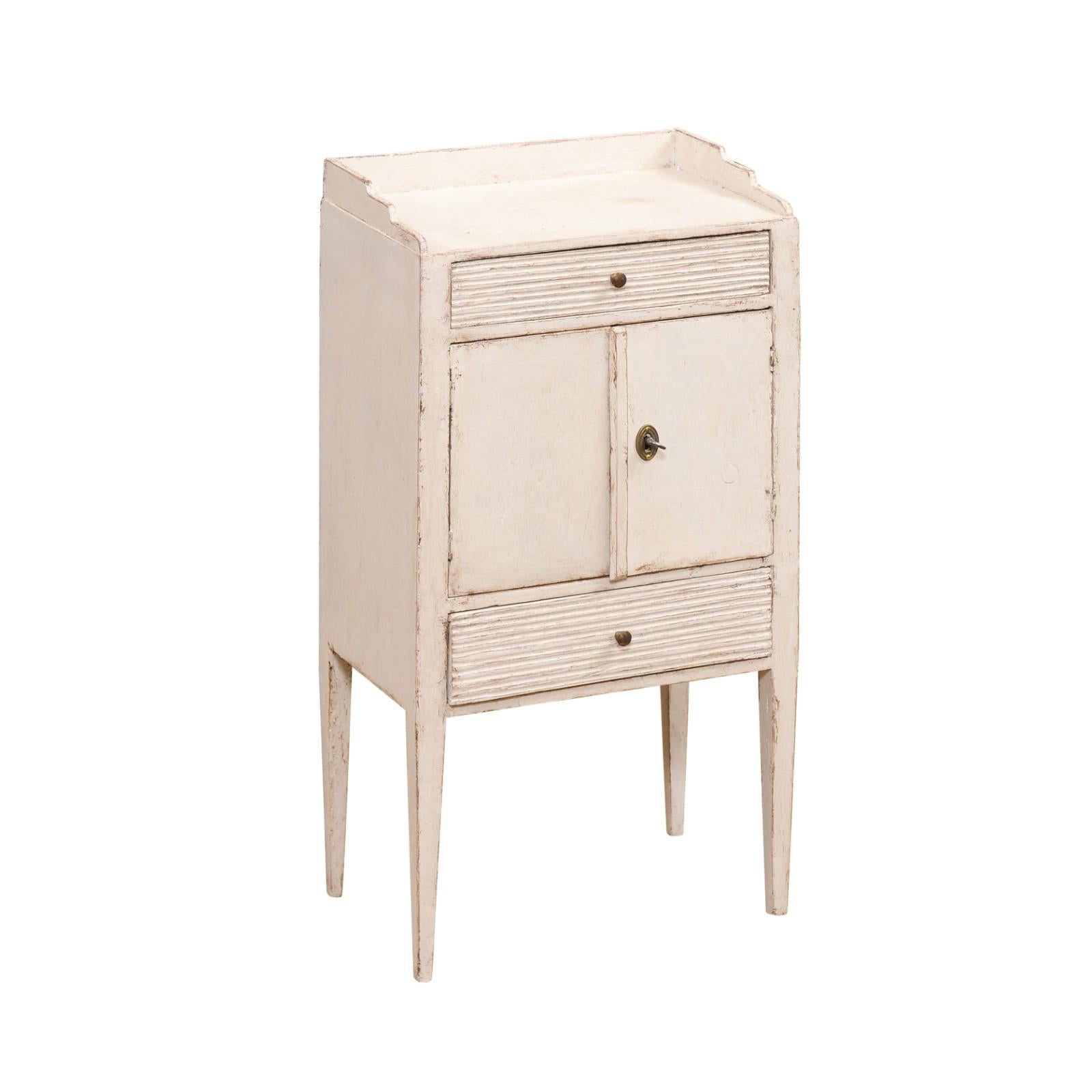 A Swedish late Gustavian painted wood bedside table from the early 19th century, with two reeded drawers, double doors and three quarter gallery. Created in Sweden during the first quarter of the 19th century, this bedside table showcases the