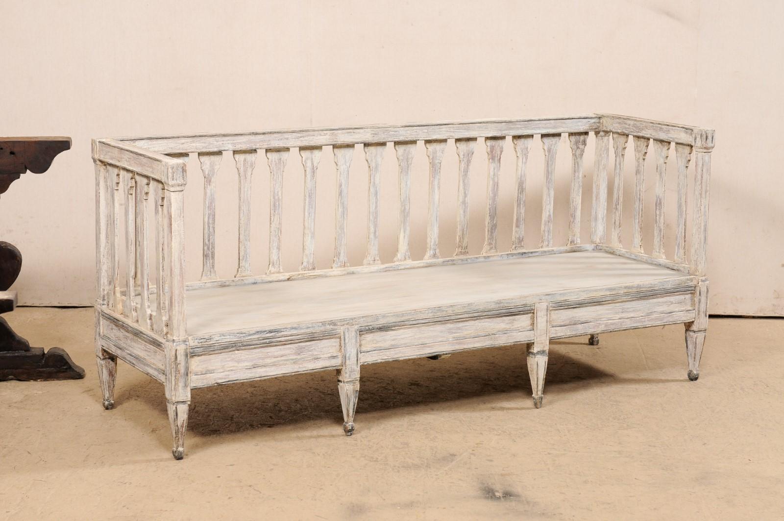 A Swedish late Gustavian Period carved and painted wood sofa bench from the early 19th century. This antique sofa bench from Sweden features a high back and arms comprised of a linear top rail with flattened, column-style carved slats set across the