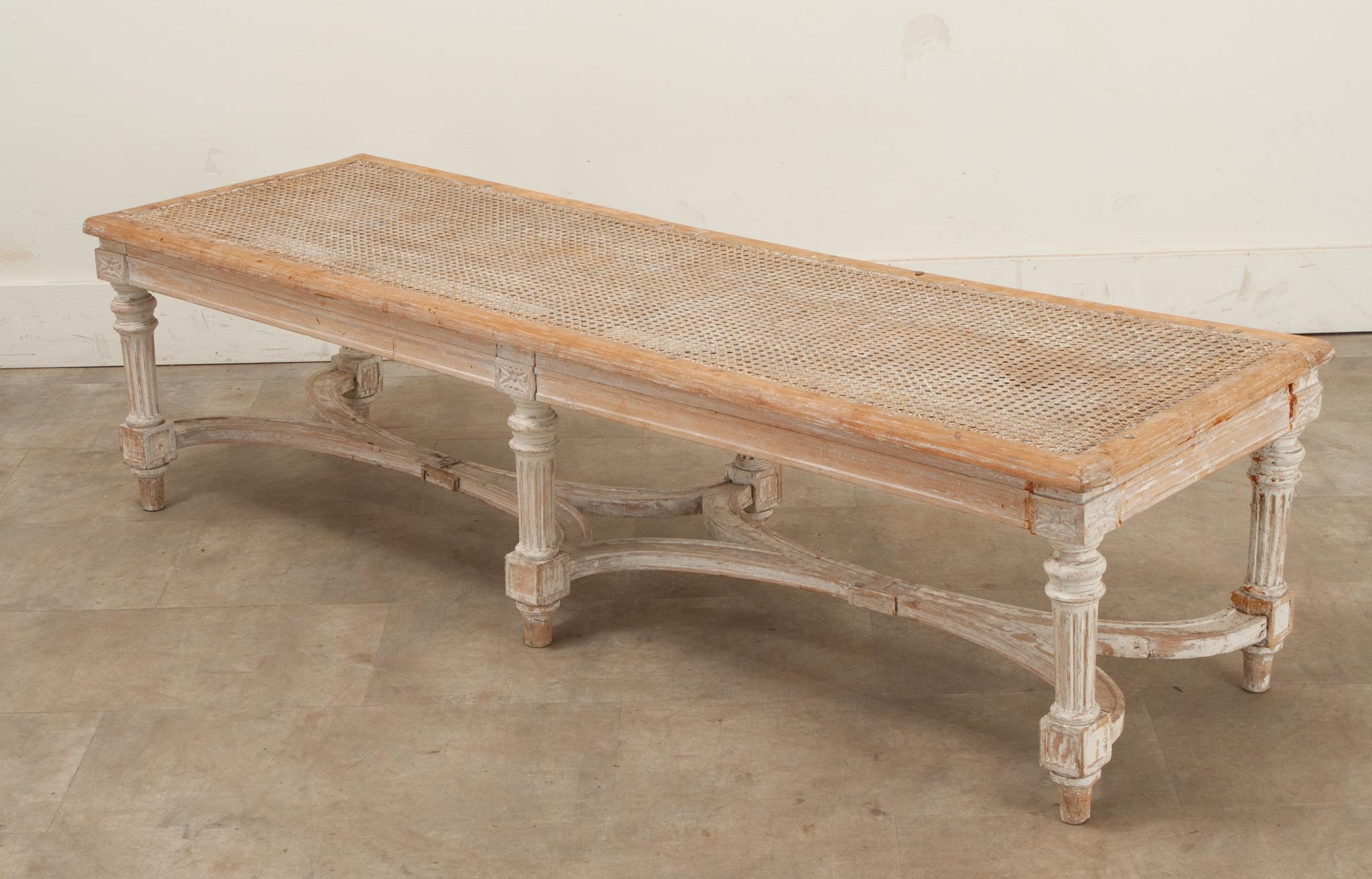 A long Swedish Louis XVI style bench, perfect at the end of a king bed. This top of this antique bench is made of cane with a light white-washed wood frame. This sturdy bench has six fluted legs that connect with a shaped stretcher. Be sure to view