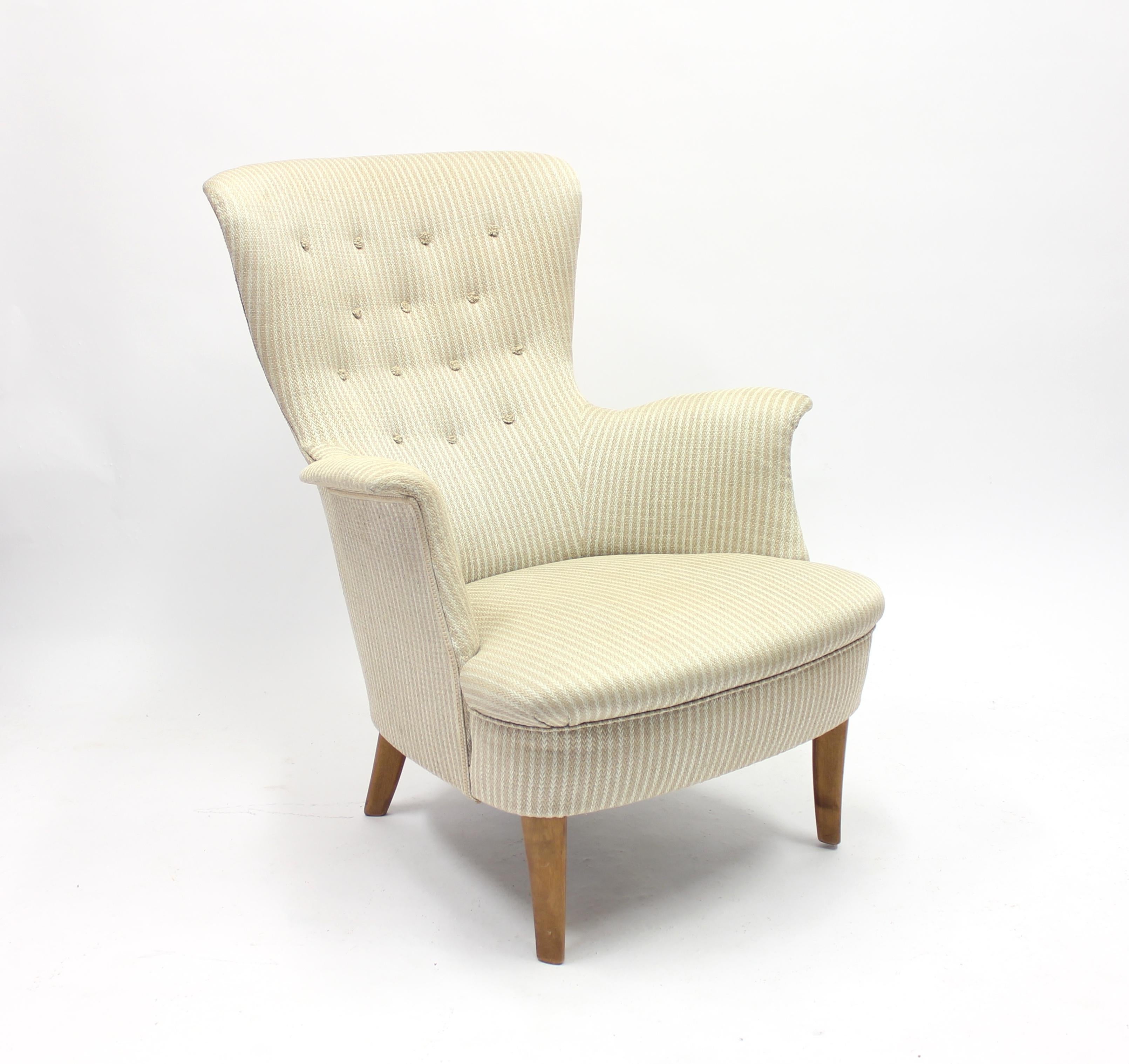 Rare lounge chair by Carl Malmsten, Sweden, 1950s. Upholseter in a striped light brown and white/beige fabric, legs made of stained birch. Stamped CM (for Carl Malmsten) on right back leg.