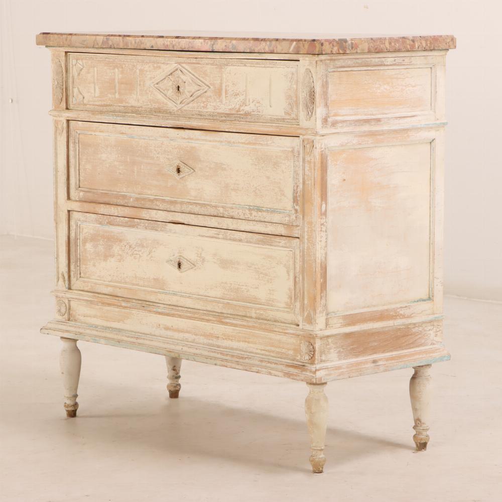 This commode has a case with three drawers, carved details throughout, turned legs, and remnants of old paint. A warm, natural finish make the chest look well loved, but the neutral surface will fit nicely in both contemporary and antique