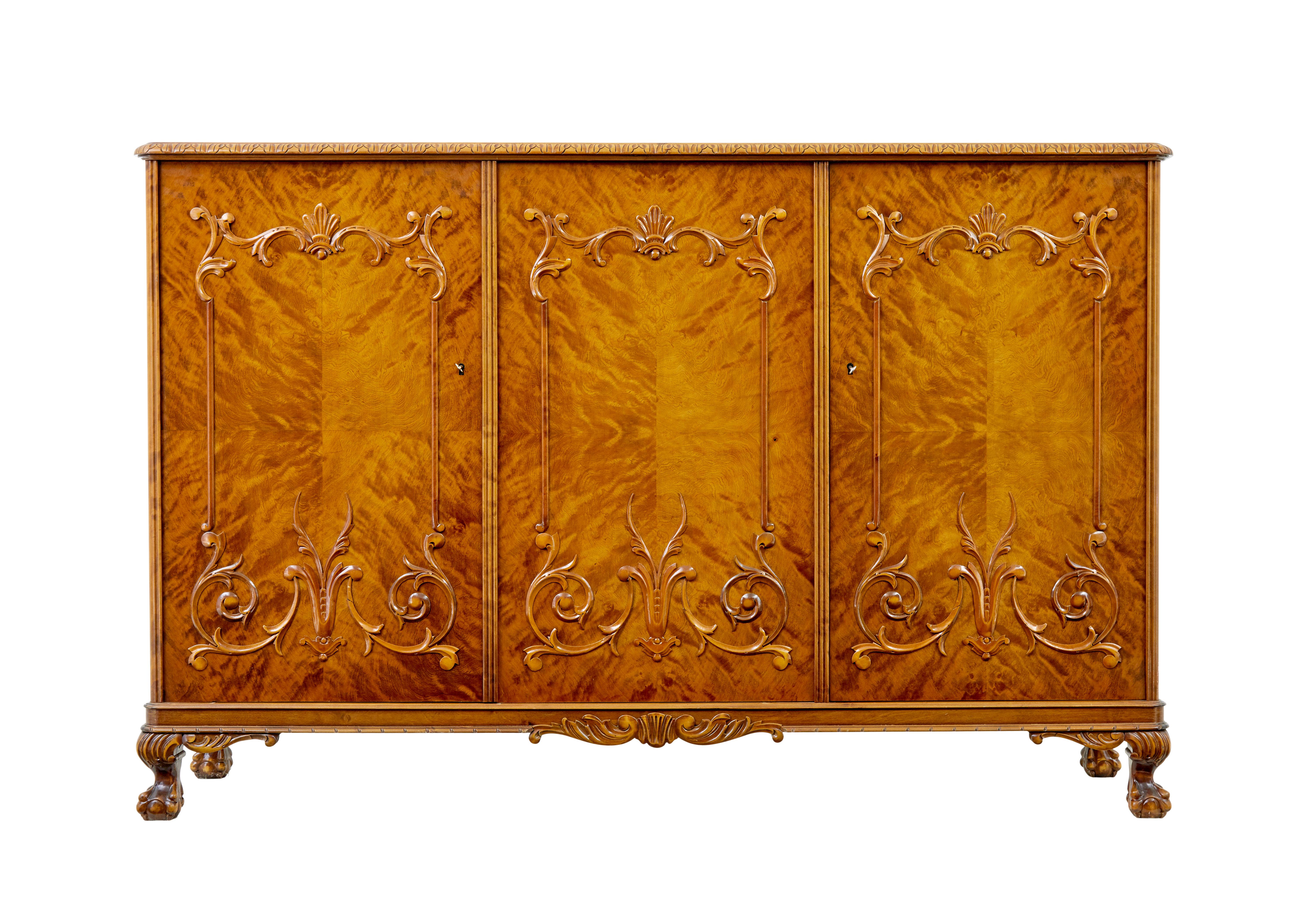Good quality Scandinavian birch sideboard in the rococo taste circa 1940.

Comprising of a single door and a double door compartment.  Top surface with decorative carved edge leads to the quarter veneered doors with applied swag mouldings.

Single