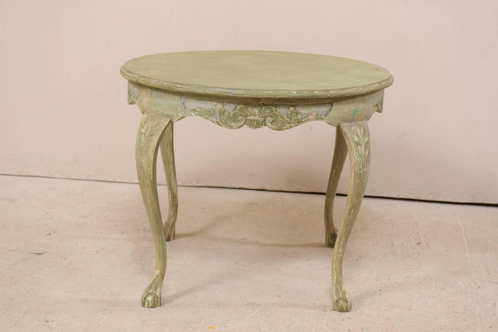 A Swedish Rococo style round painted wood table from the mid-20th century. This vintage Swedish table features a circular-shaped top with nicely carved and gently scalloped apron, adorn with shell and leaf motifs at the skirt's centre on all sides,