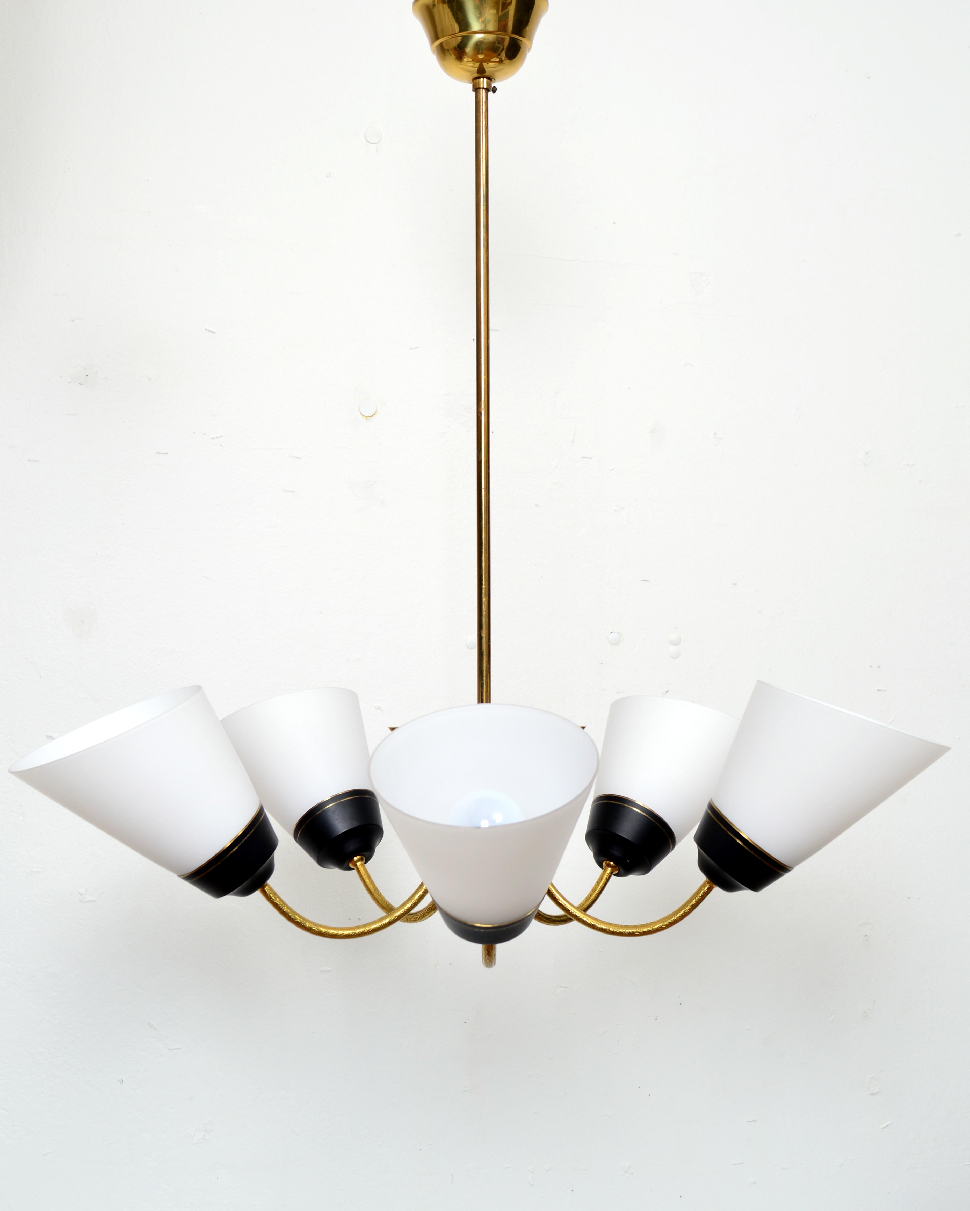 Lustre moderniste scandinave en laiton, composé de cinq bras courbés supportant des abat-jours coniques en verre opale. Les abat-jour sont en parfait état et fixés par des ferrures métalliques avec des anneaux décoratifs en laiton. Il est livré avec