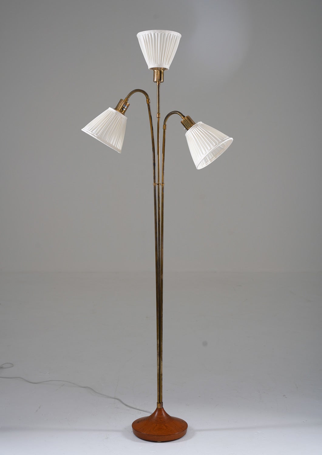Lovely three-armed floor lamp manufactured in the 1960s. 
This lamp is made of brass with a foot in solid teak. It features three light sources, hidden behind new hand-pleated chintz fabric shades, held by adjustable arms.

Condition: Very good