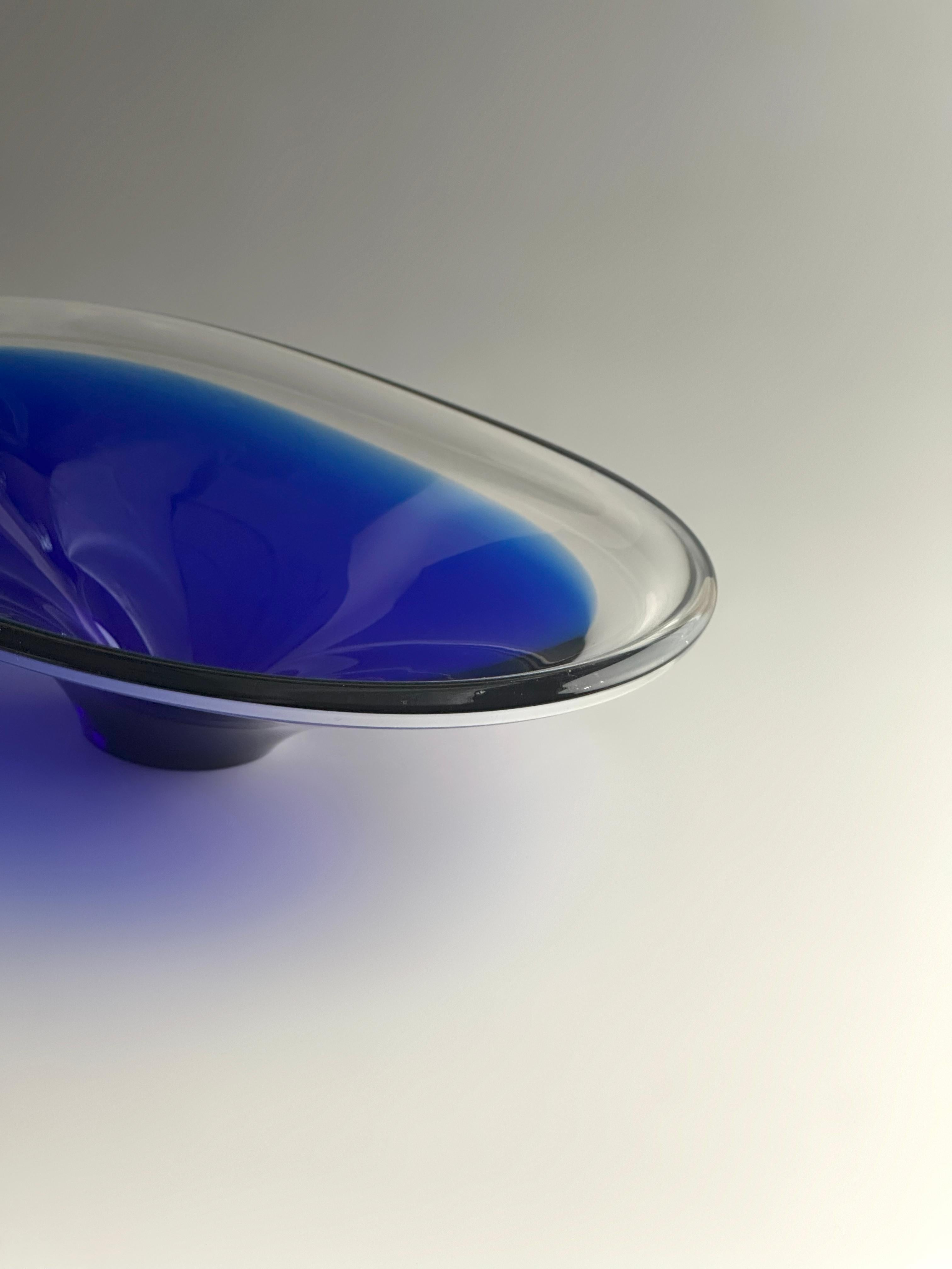 A mid-century decorative art glass bowl, hand-crafted in Sweden during the 1960s. This striking piece combines deep cobalt blue glass with a casing of clear, sparkling crystal, resulting in a vivid interplay of colour and transparency that
