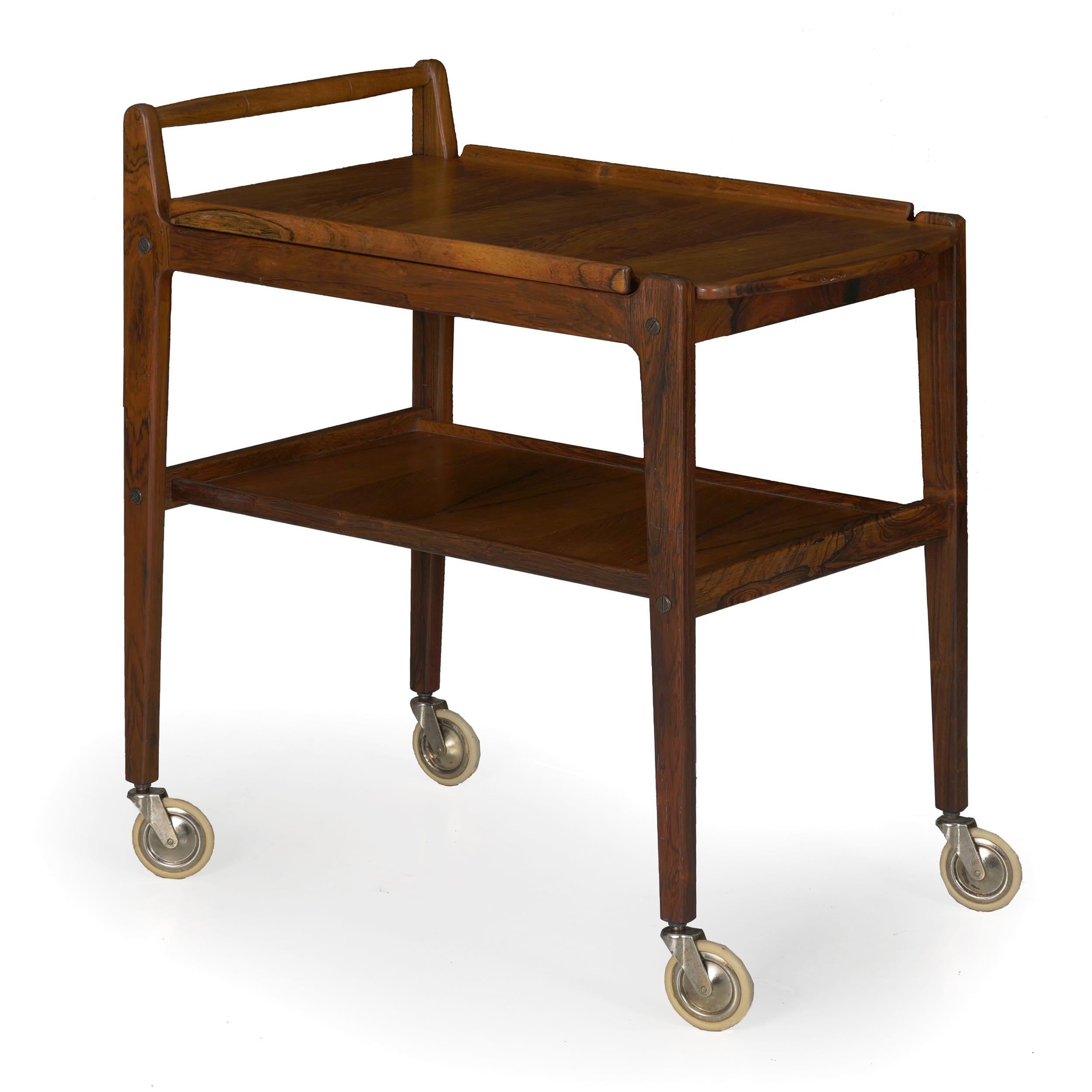 A gorgeous midcentury bar cart designed by Erik Gustafsson and manufactured in Sweden, it is crafted in rosewood solid and veneers. The tray top has a nice molded edge and is removable, convenient for serving food to the living areas. It rolls over