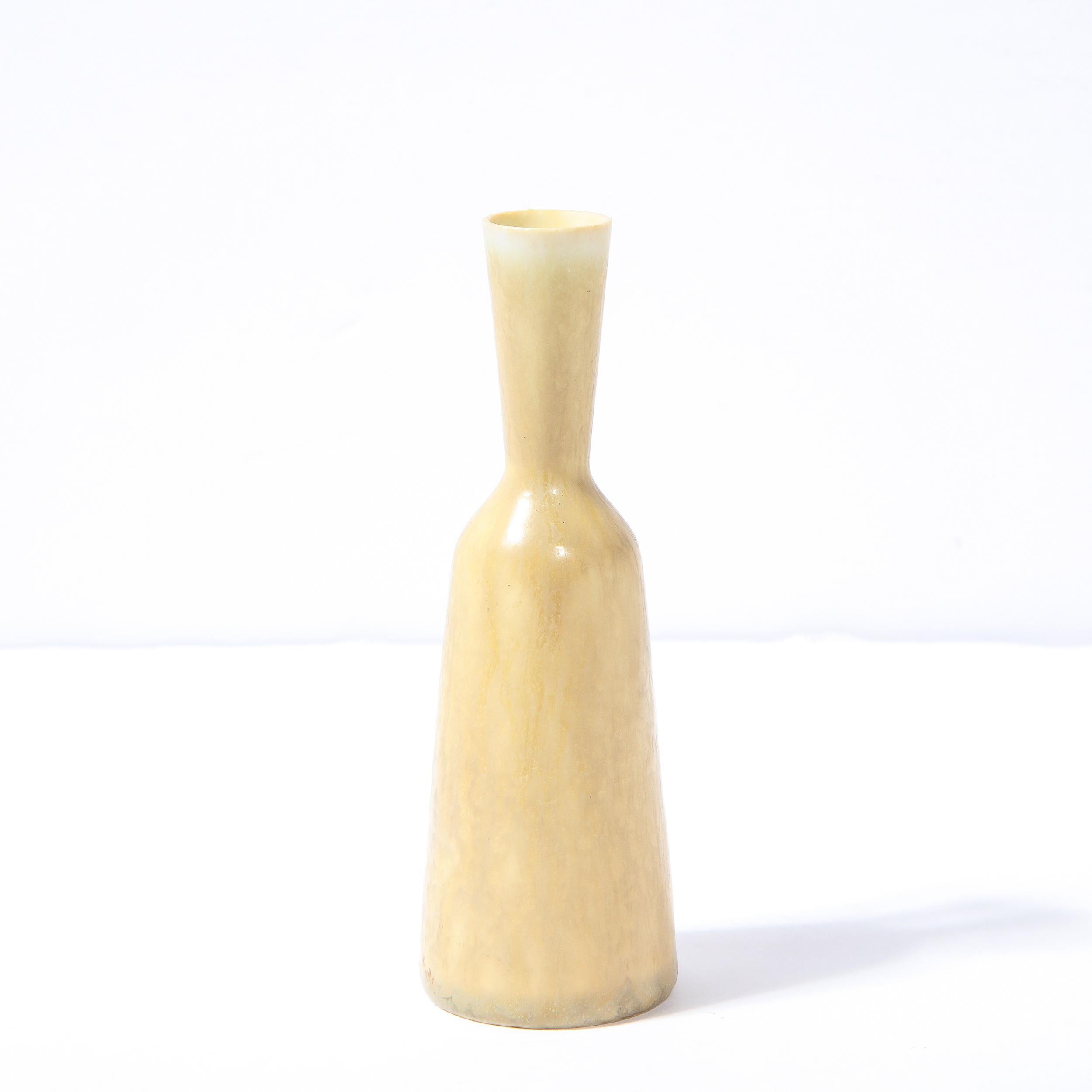 This elegant Mid-Century Modern vase was realized by Gunnar Nylund for Rorstrand in Sweden circa 1960. It features an hourglass form tapered body in glazed ceramic in a sophisticated sand hue with a sculptural handle and a flared neck culminating in