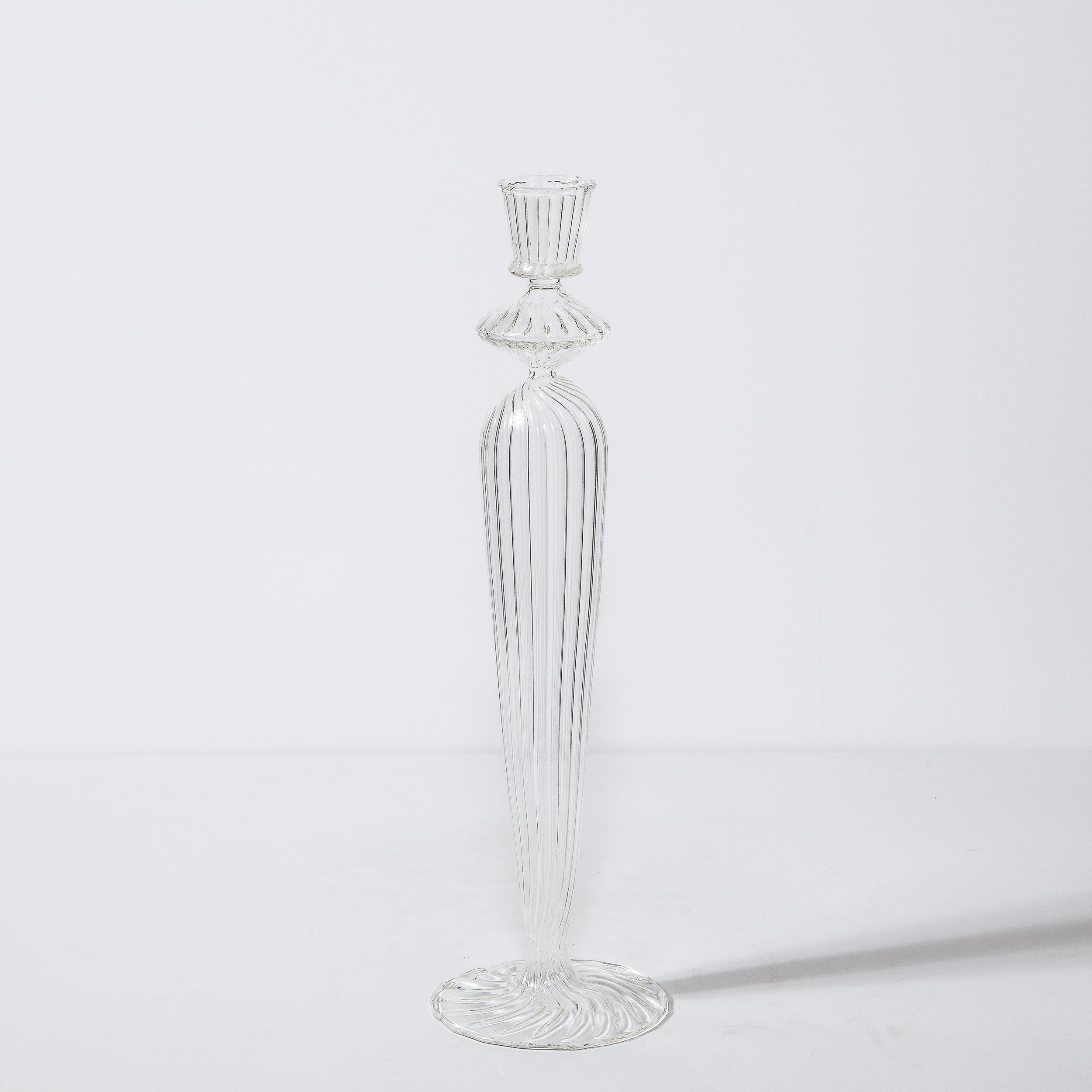 This elegant Mid-Century Modern candleholder was realized in Sweden, circa 1960. It features a tapered and undulating cylindrical body with a circular mouth and base all in translucent channeled glass. With its beautiful craftsmanship and clean