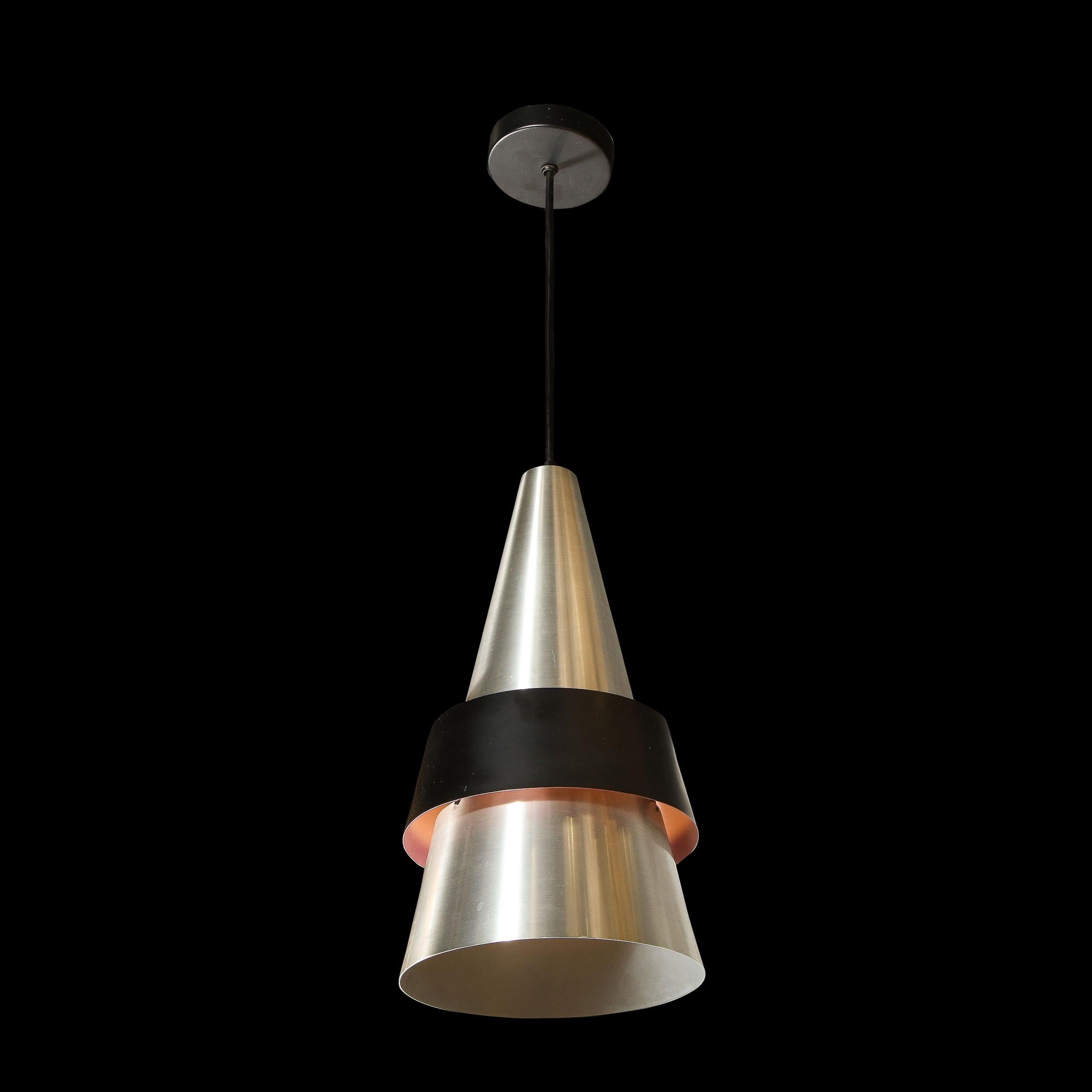 This stunning mid century pendant was realized in Sweden circa 1960. A conical brushed aluminum shade- split into two segments- hangs suspended. The break in the the two parts of the cone is covered by a band- a ribbon like band in black enamel that