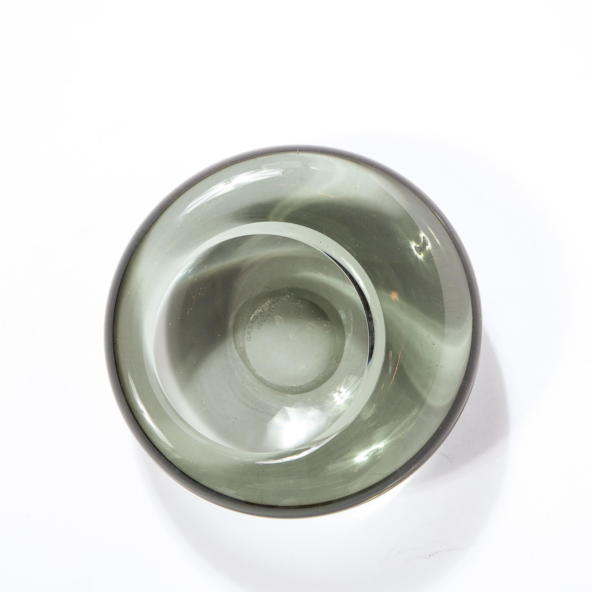 This stunning Mid-Century Modern smoked glass dish was realized by the celebrated atelier of Holmegaard in Sweden in 1958. It features a sculptural circular body with slightly off set central depression- all in beautiful smoked translucent glass.