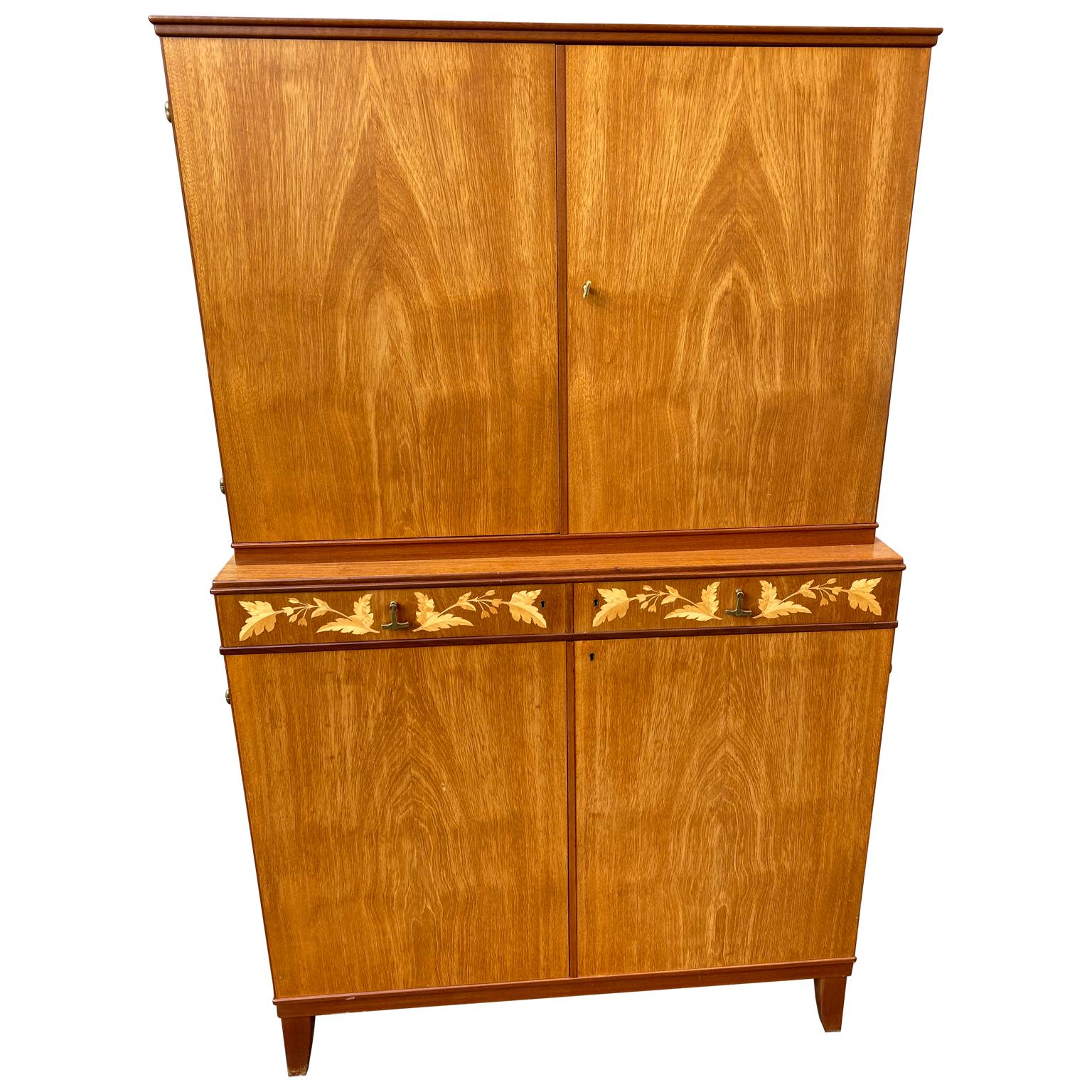 A sharp looking Swedish-made cabinet by J.O. Carlssons.
The cabinet has two drawers with original brass hardward and citrus veneer inlaid flower decorations. It is in good sturdy condition. Lower part of the cabinet has options for two shelves,