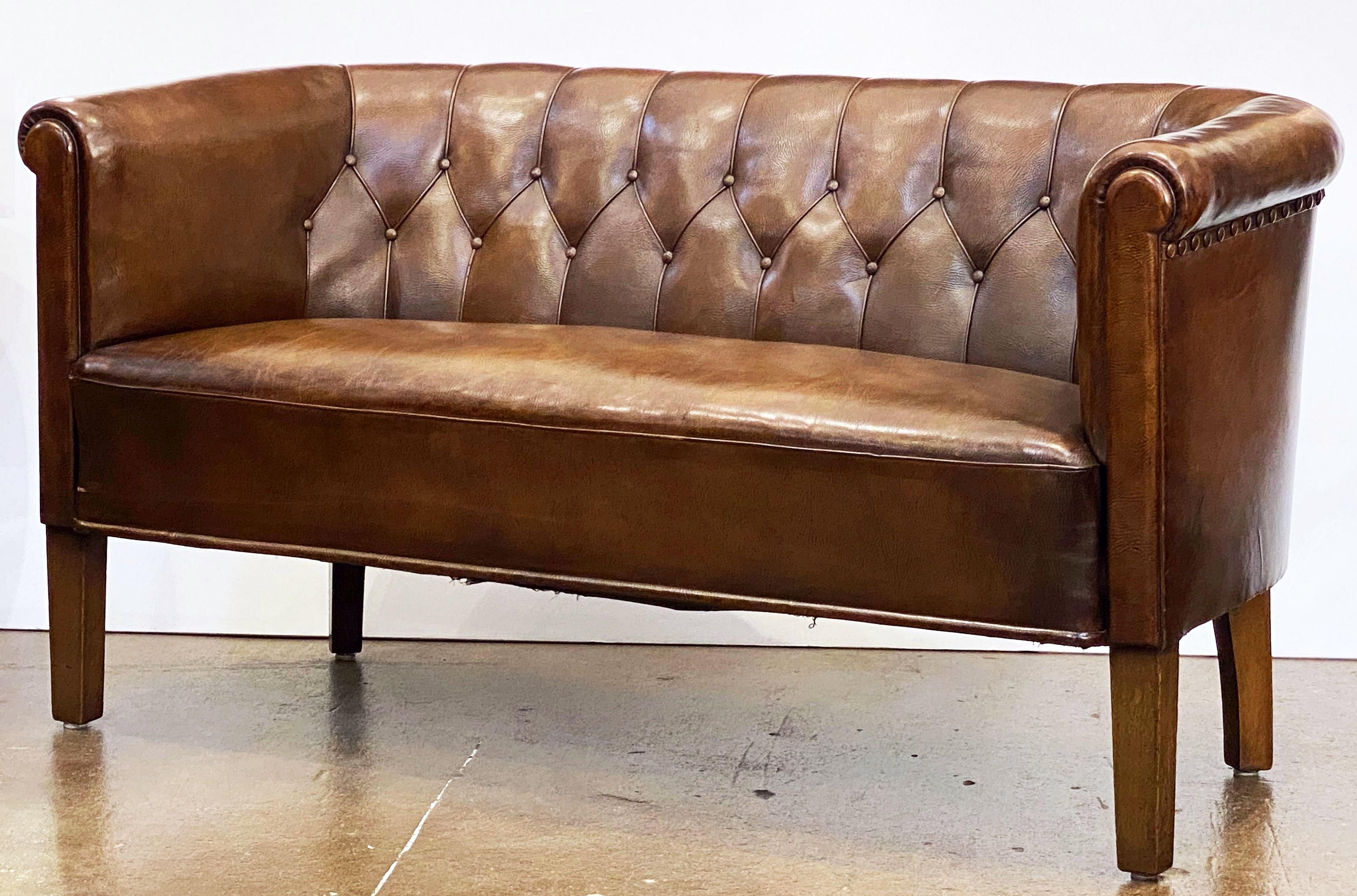 A fine Swedish leather sofa or settee from the Mid-Century Modern era, featuring a tufted back and stylish arms, with a comfortable seat resting on four shaped legs, and decorative nail-head trim accents around the backside.
