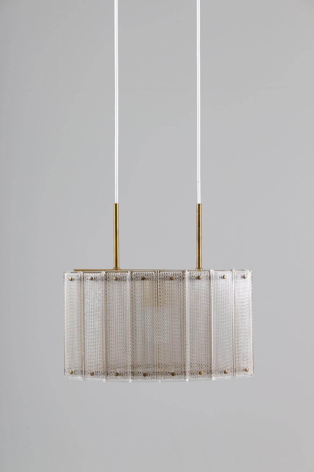 A high-quality pendant produced by Falkenbergs, Sweden. 
The construction of this lamp is very minimalistic and elegant. Two brass rings hold a perforated metal cylinder, which is surrounded by glass blocks that are held in place by brass screws to