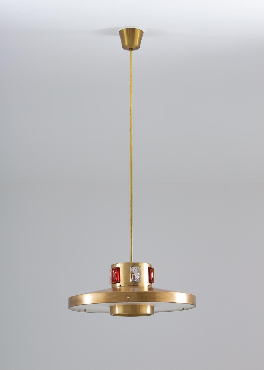 Swedish midcentury pendant by Einar Ba¨ckstro¨m, 1960s.
This pendant is made of brass-coloured metal with white and red glass blocks. The glass blocks lit up beautifully when the lamp is lit and the metal has a beautiful patina.
The length of the