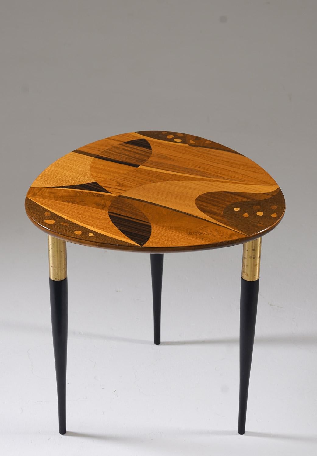 A striking Swedish side table from the 1950s, featuring an exquisite intarsia tabletop crafted from a variety of richly grained woods. The intricate marquetry design showcases organic, flowing shapes in contrasting wood tones, highlighting the
