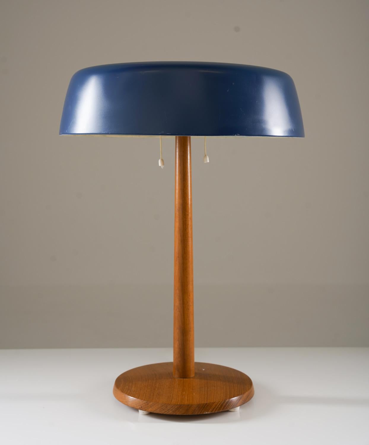 Lámpara de sobremesa de teca y metal pintado de azul, fabricada por Bergboms en Suecia durante la década de 1960.
 La lámpara presenta una elegante base de teca suavemente ahusada que sostiene una amplia pantalla metálica ligeramente curvada en