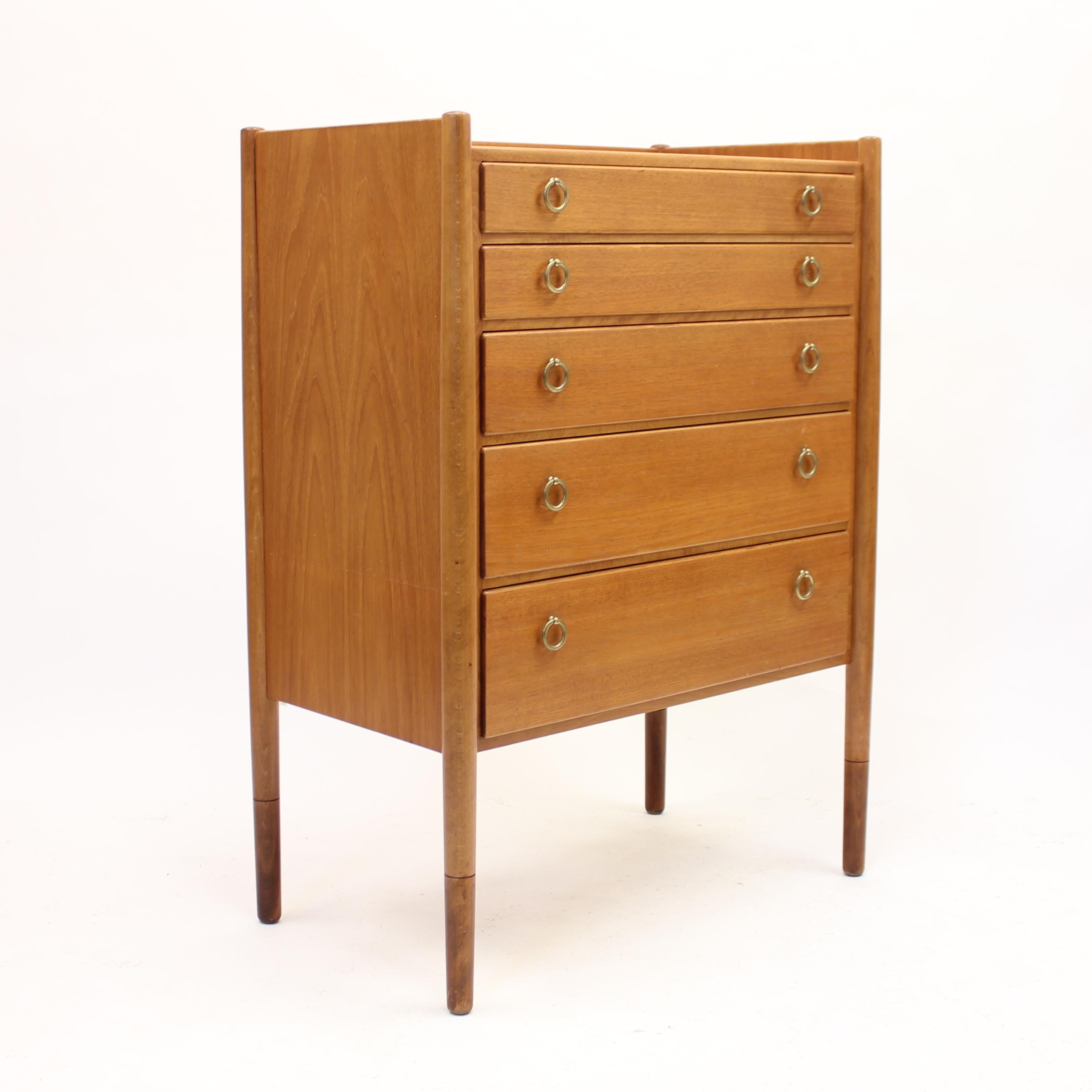 Mid-century teak chest of drawers with 5 drawers and round brass handles made by Swedish company Treman in the 1960s. The lower part of the lags has a darker staining which makes a nice contrast between that and the rest of the chest. It's a bit