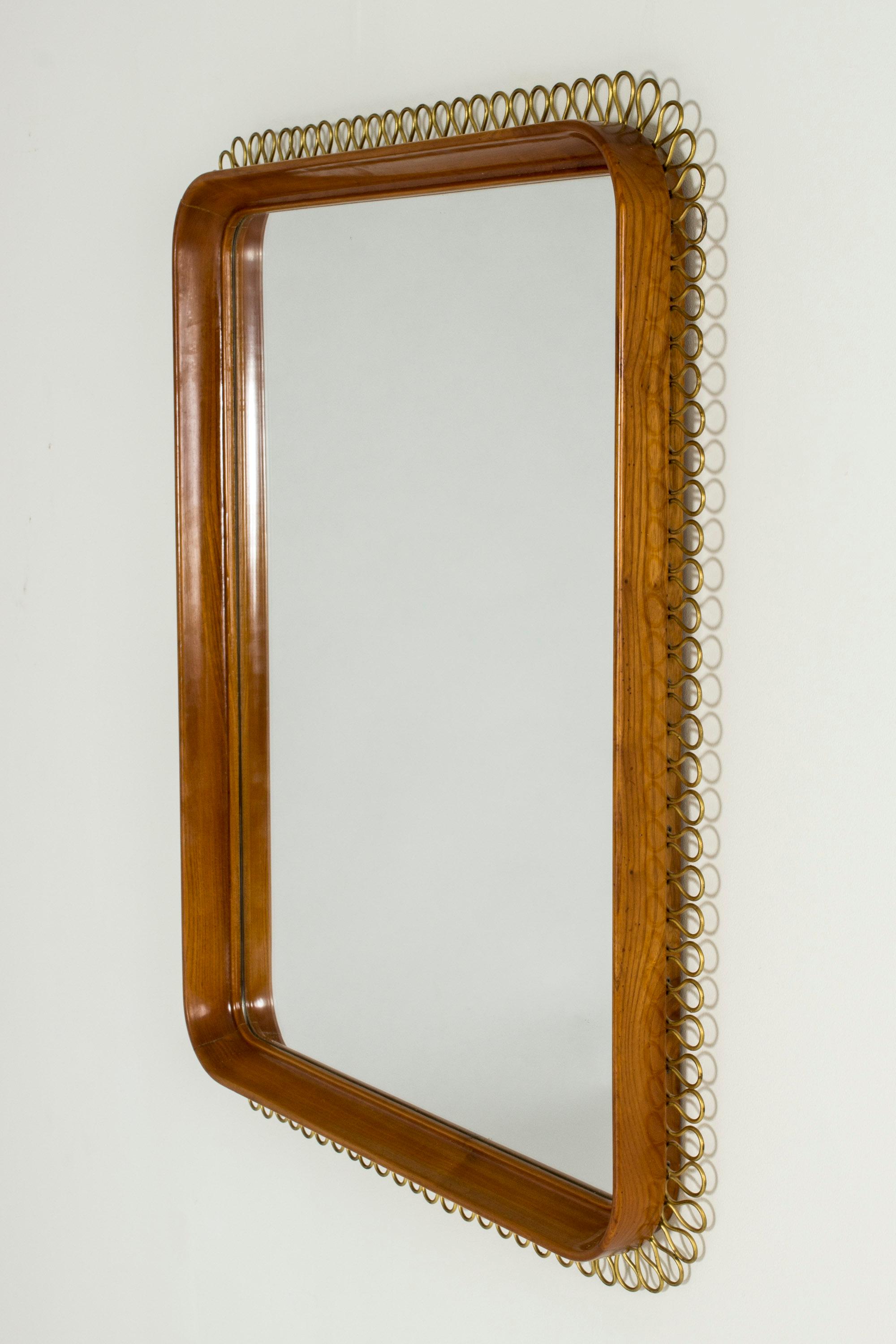 Beautiful wall mirror with a mahogany frame and decorative wave of brass wire around the edge. Elegant style in the manner of Josef Frank.