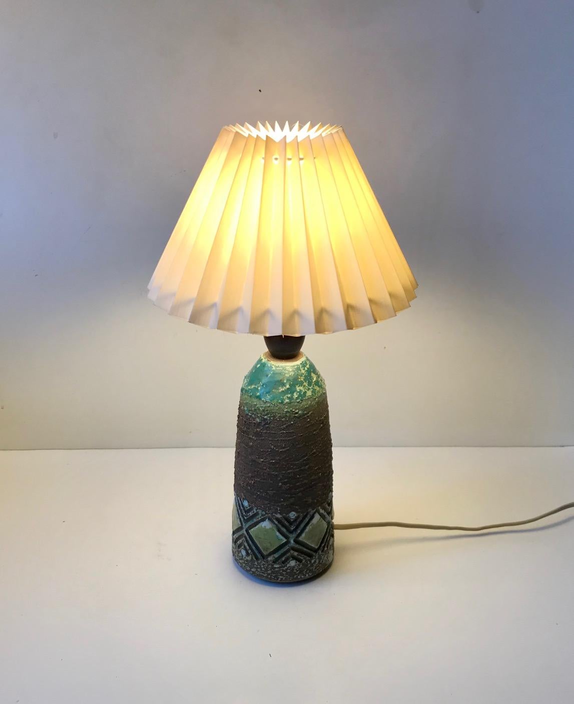 An earthy brown table light decorated with diamond patterns and splashes of turquoise, green and white glazes. It was designed by Gertrud Hertner and made at Tilgmans Keramik in Sweden circa 1960-65. The light features on/of switch to its bakelite