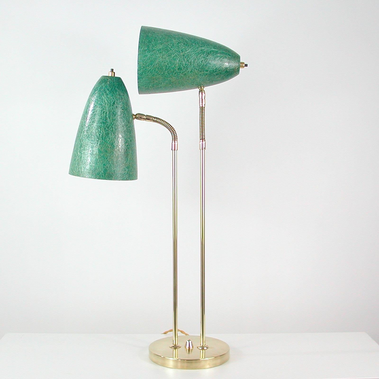 This unusual desk lamp was designed and manufactured in Sweden in the 1950s. It features a brass lamp base, brass lamp rods and two adjustable cone shaped lamp shades made of green fiberglass. The lamp shades can be turned in any possible direction.
