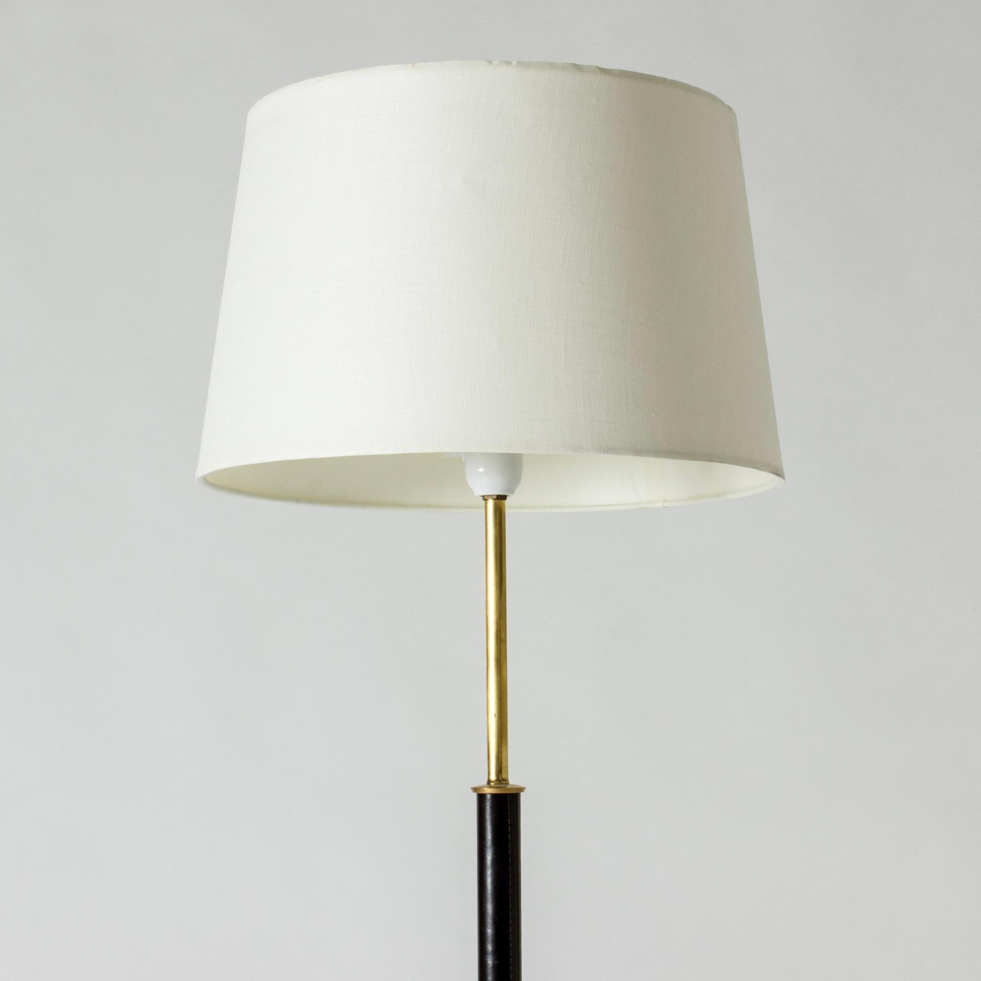 Elegant midcentury floor lamp, made from brass with a leather dressed stem. Black lacquered base.