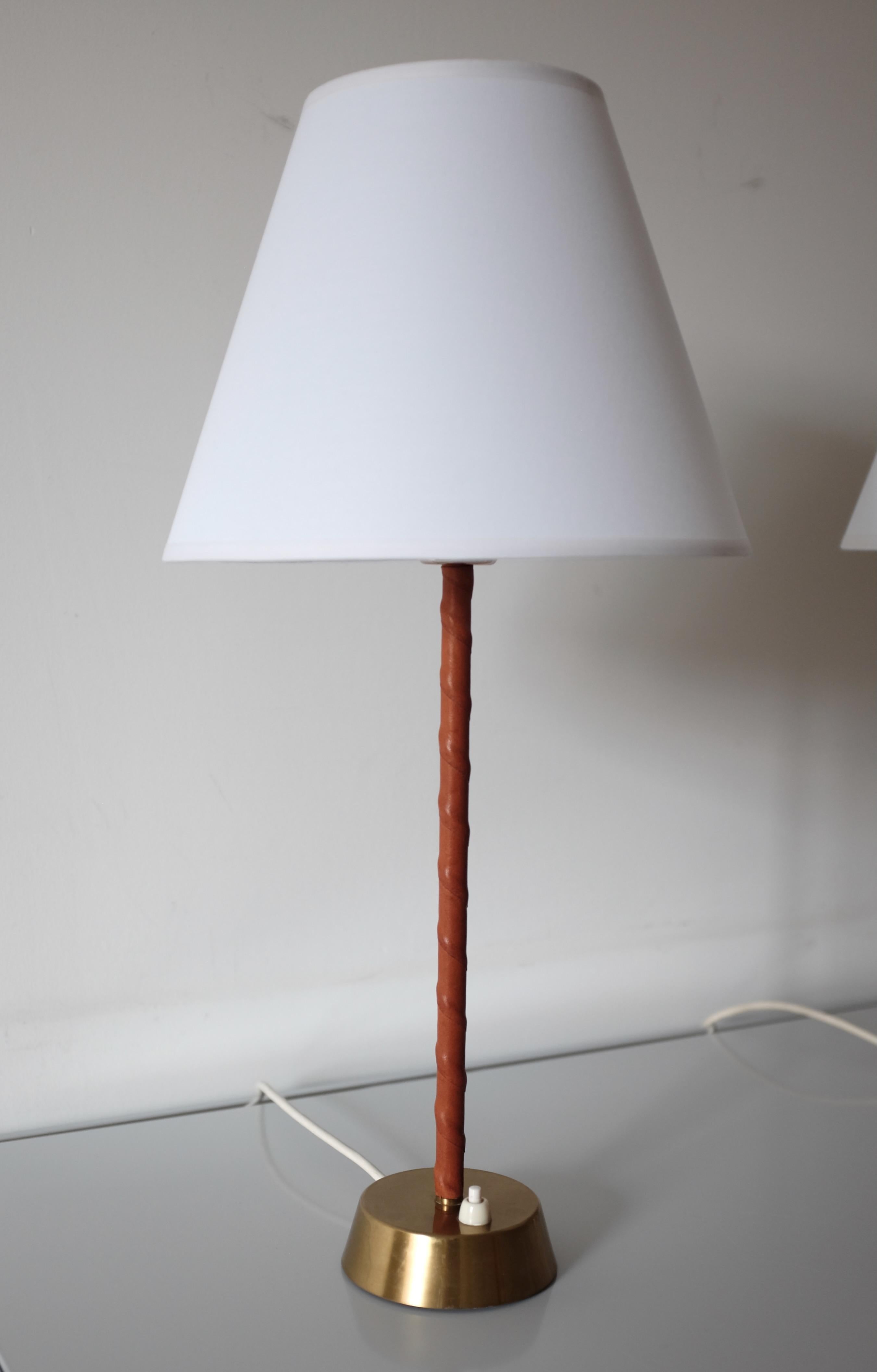 Pair of Swedish midcentury Table lamps by ASEA Skandia. Brass lampfot and leather covered lamparm with new white linen lampshades. Stamped with Model number 116 underneath with makers name. Very good working condition with age appropriate wear to