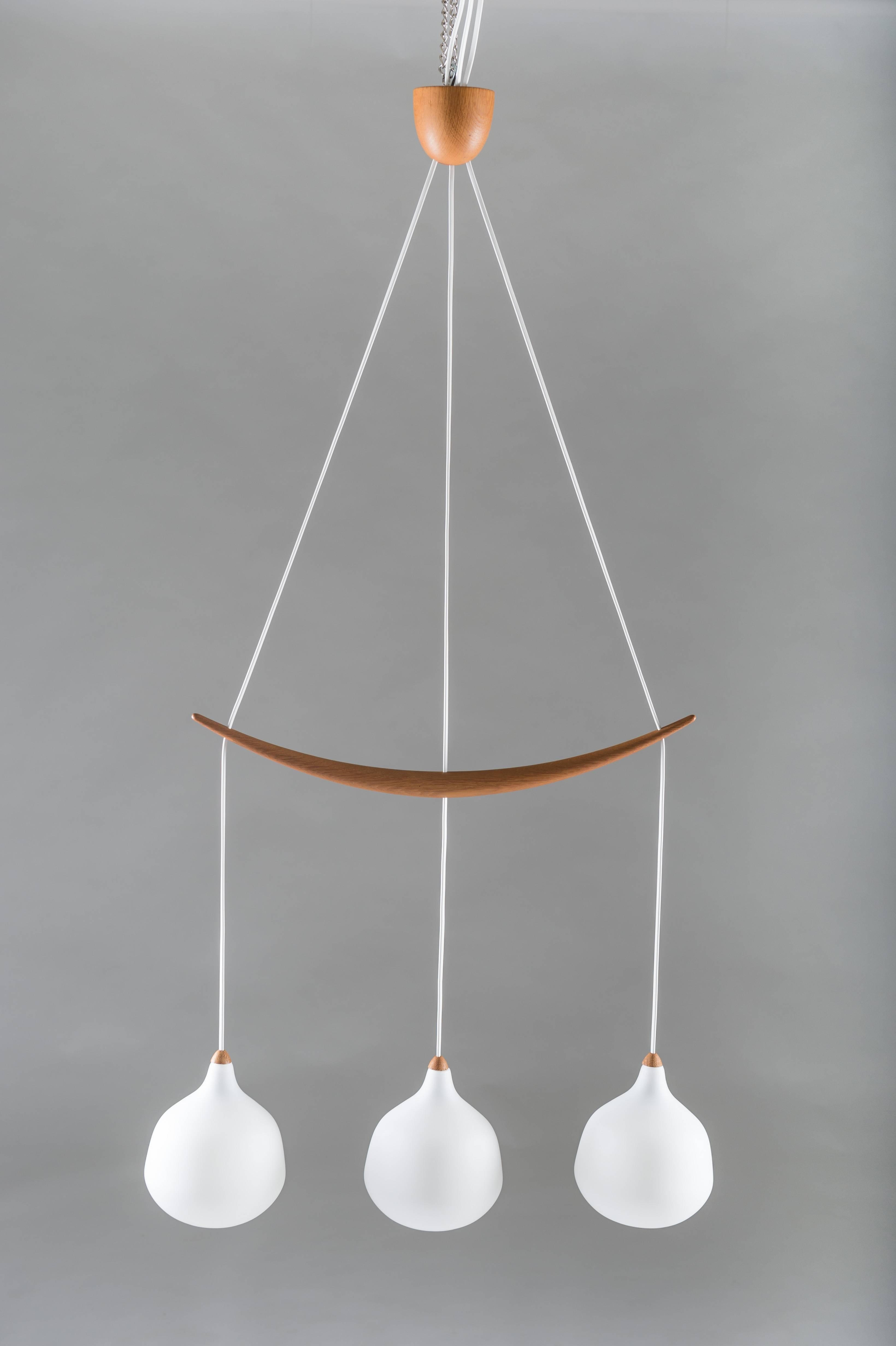 Pendant in oak and opaline glass by Uno and Östen Kristiansson for Luxus. The lamp features three hanging glass spheres, divided by a carefully carved oak stick. 
Condition: Excellent.