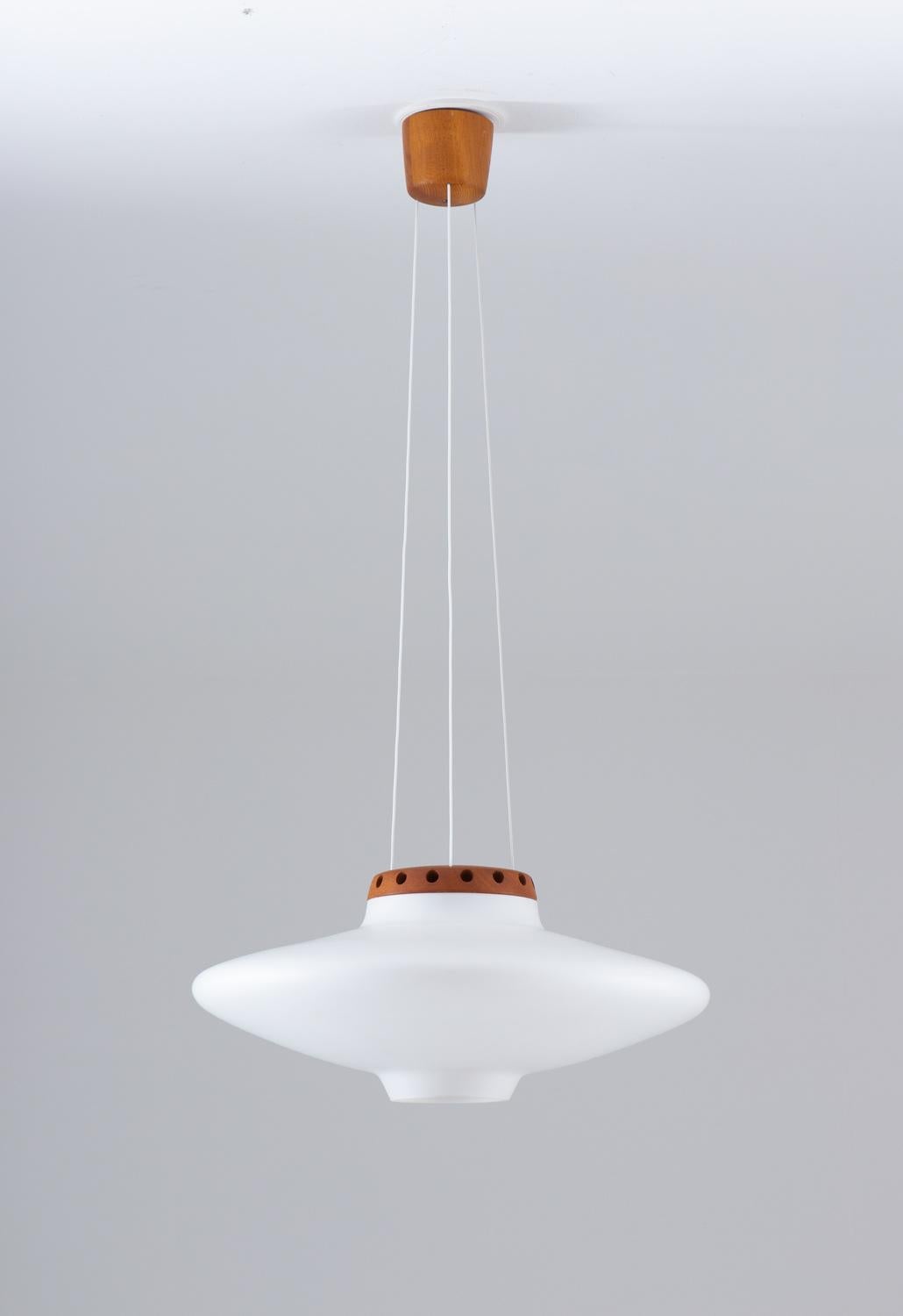 A pendant by Uno and Östen Kristiansson for Luxus, 1950s. This lamp features a large sphere in frosted opaline glass, held by a teak piece with small holes around it that lets the light out in a beautiful way against the ceiling. Three wires are