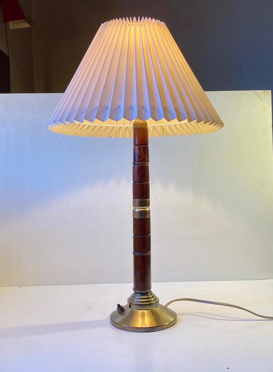 A large stylish Swedish table light composed of af white fluted shade, a architecturally stained brass base and a stem set with 'rings' in mahogany with brass accents. This type of Mahogany is not restricted in Cites. It was made in Sweden during