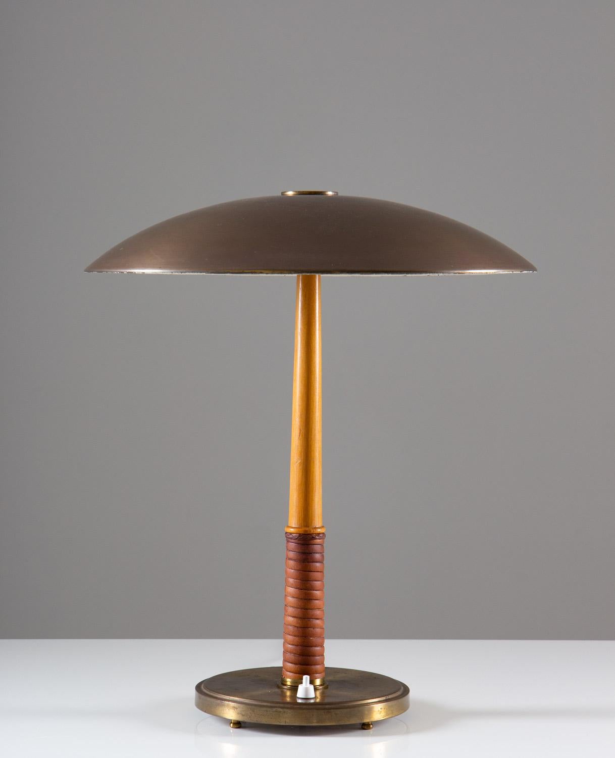 Rare table lamp in brass, leather and wood, by Böhlmarks, Sweden.
This elegant lamp was manufactured during the Swedish Modern era and is of very high quality. It consists of a heavy brass foot, holding a leather webbed wooden base. The shade is