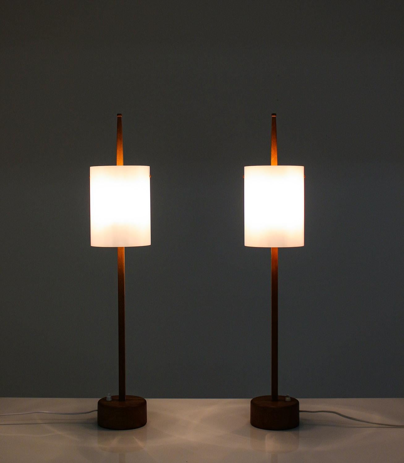Rare pair of table lamps by Uno & Östen Kristiansson for Luxus. 
The lamps consist of two light sources, hidden by an acrylic shade. The shade rests on an oak pole, which sits on a thick wooden foot with a heavy iron plate on the bottom. Very high