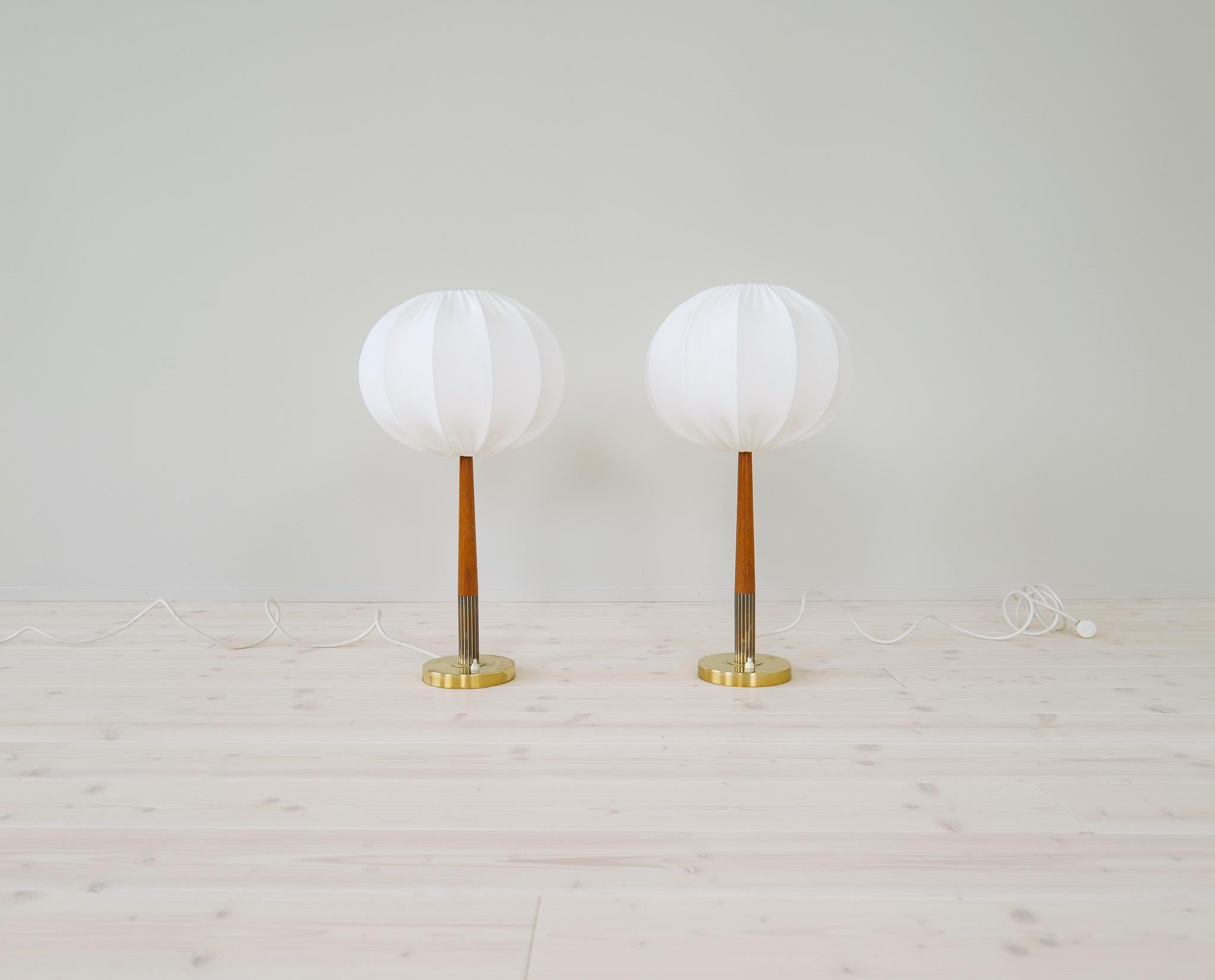 Magnifiques lampes de table en laiton et teck avec abat-jour en coton classique par Boréns, Suède.
Ces deux lampes sont un bon exemple des lampes de haute qualité produites en Suède au milieu du siècle dernier. Fournie avec des abat-jours en coton