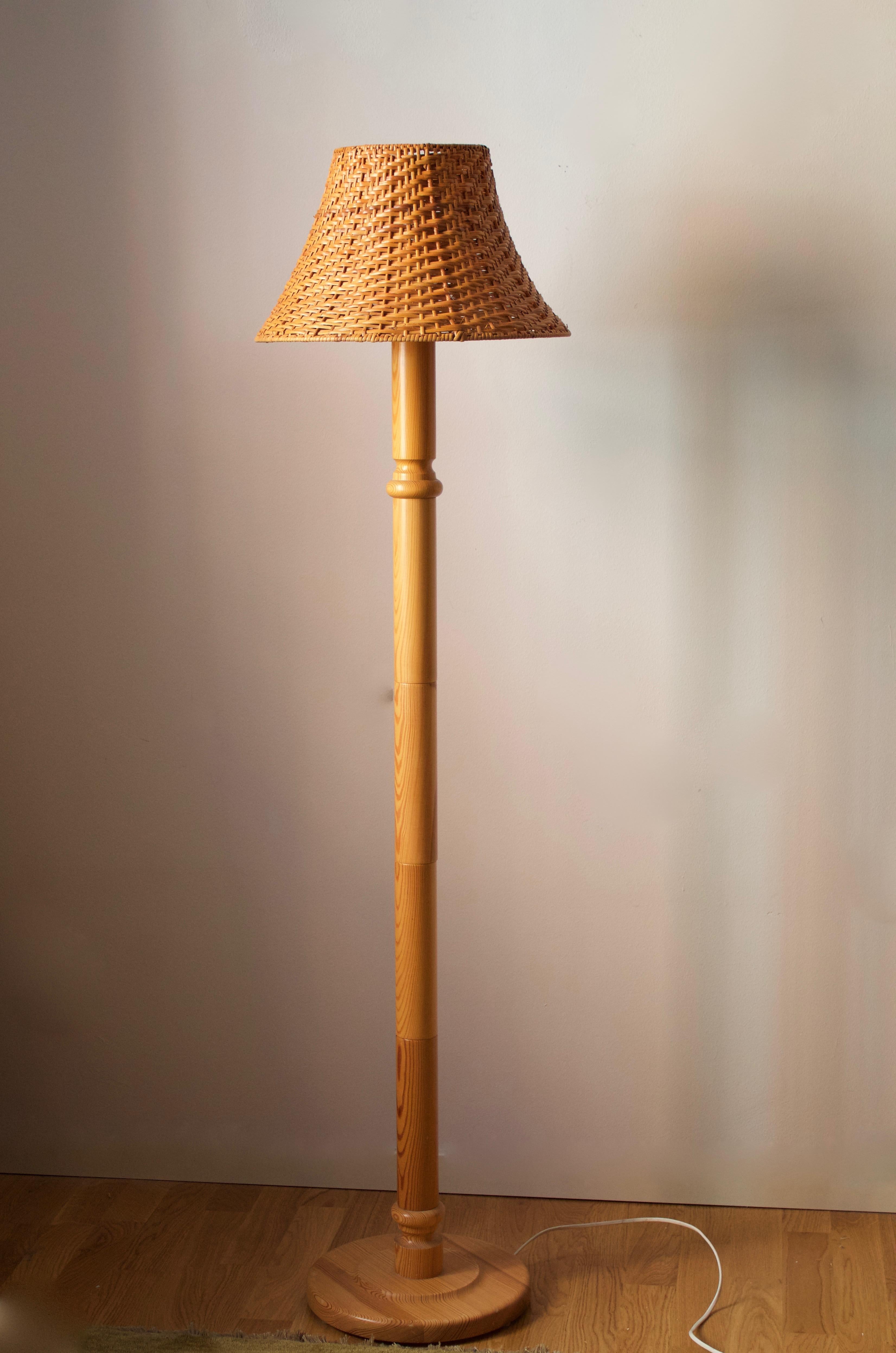 A floor lamp designed and produced in Sweden, 1970s. In solid pine. Assorted vintage rattan lampshade.