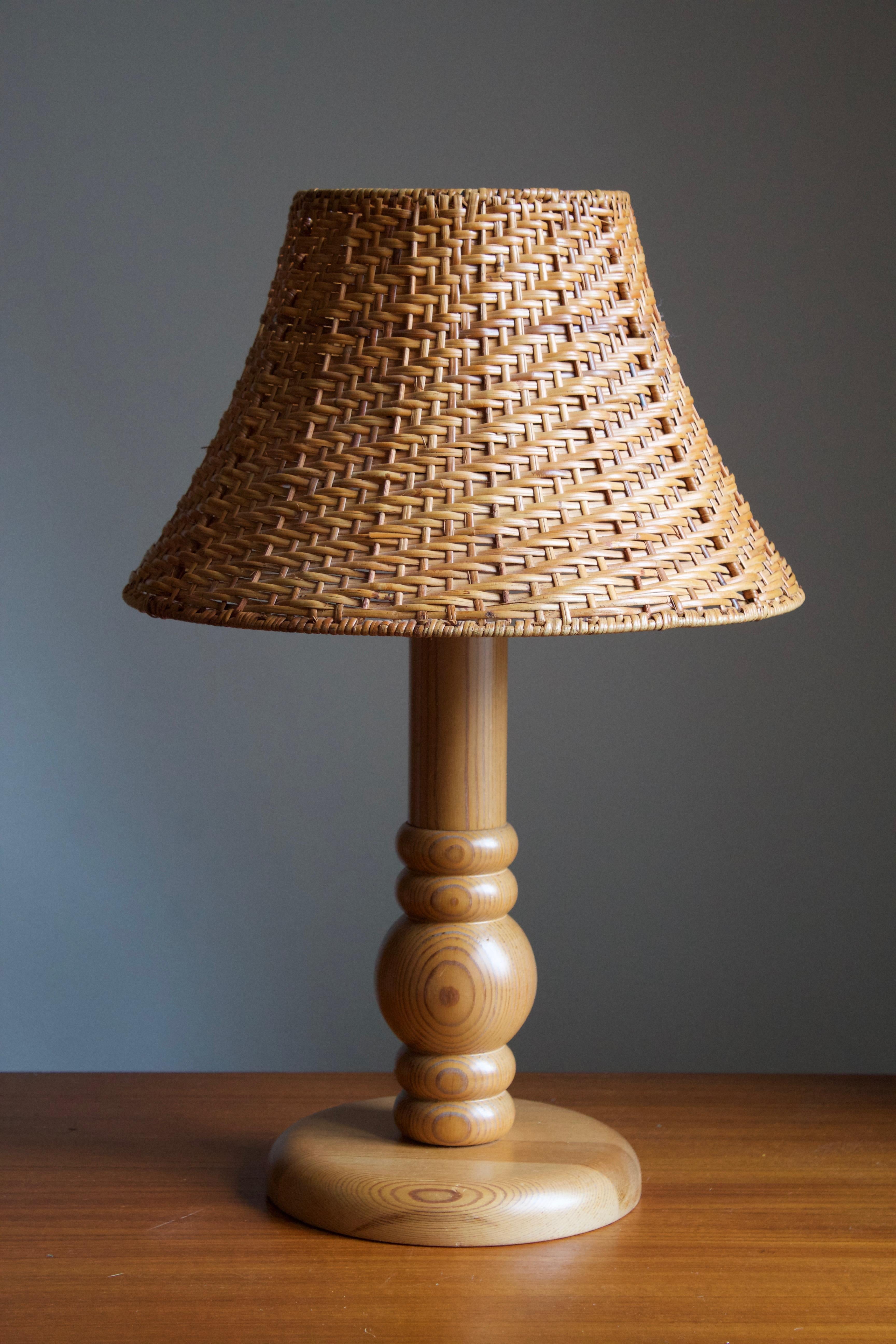 A table lamp designed and produced in Sweden, 1970s. In solid pine. Assorted vintage rattan lampshade.

Stated dimensions exlude lampshade, height includes socket. Upon request a vintage rattan lampshade of model illustrated can be included in