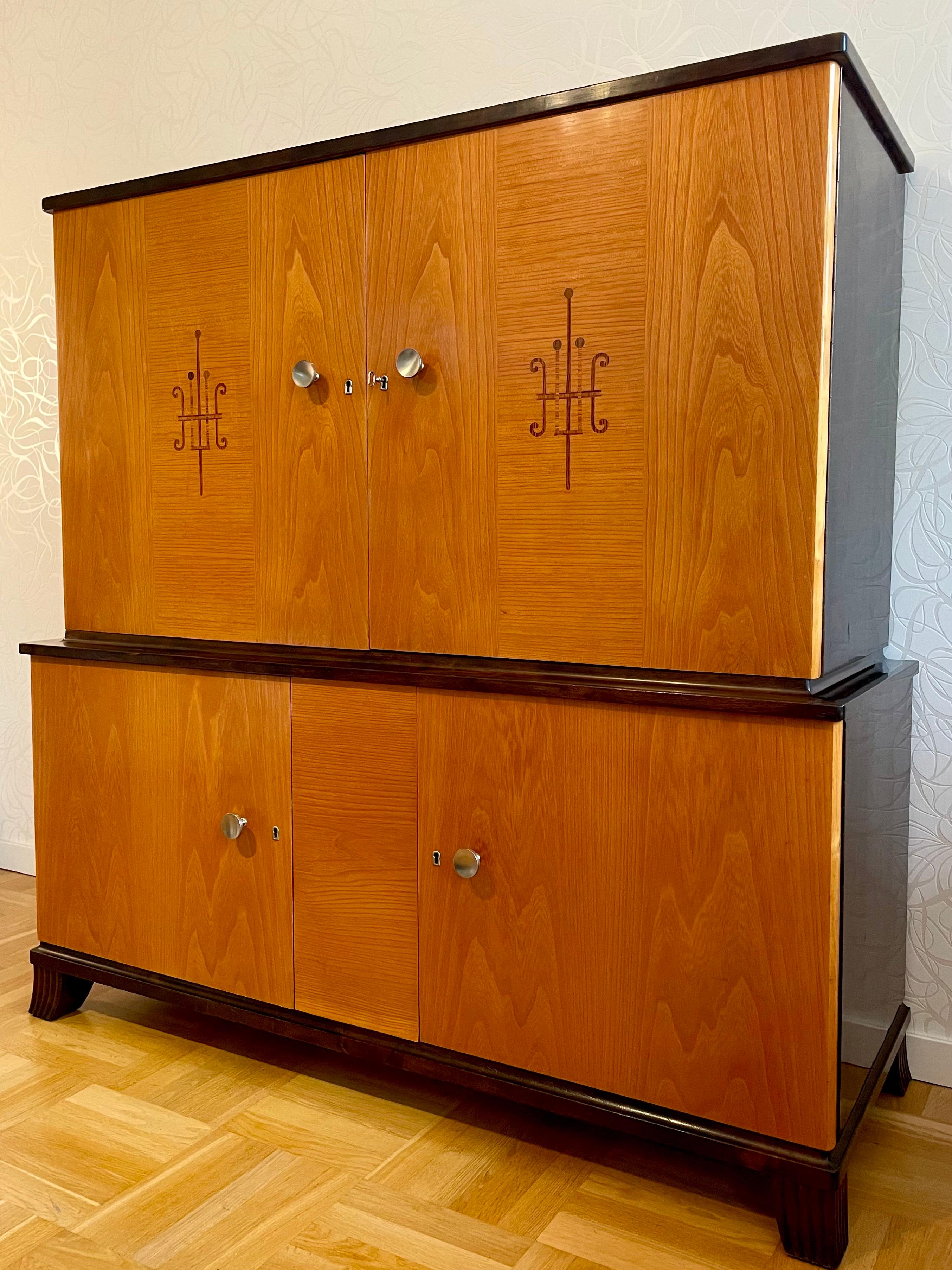 Dies ist der schwedische moderne Schrank aus den 1930er Jahren aus Ulme und Birke. 

Es wird in zwei Teilen in der Höhe gebaut. Jeder Bereich ist wiederum in zwei Stauräume unterteilt. hat jeweils zwei Türen mit beweglichen Einlegeböden.

Die beiden