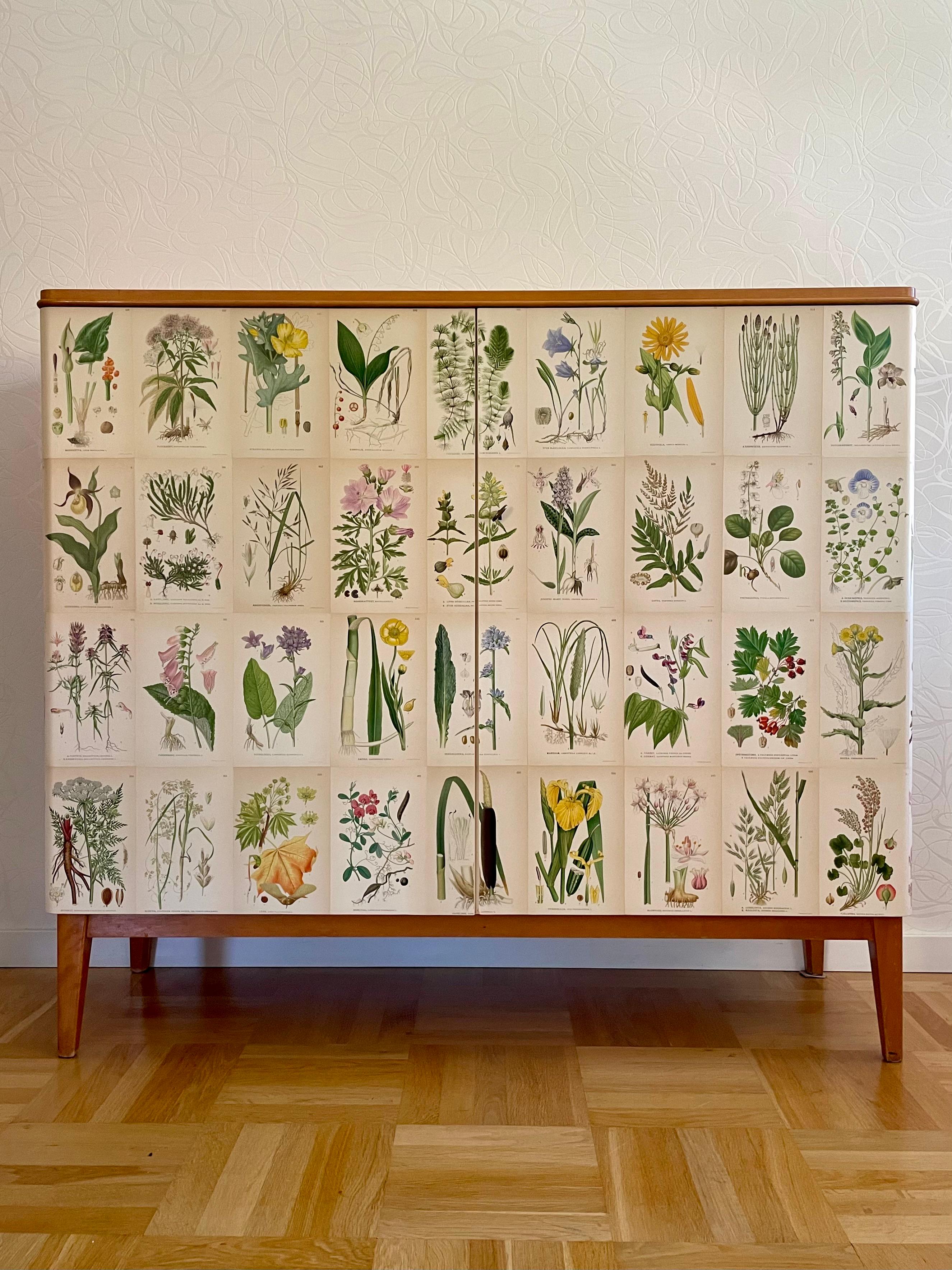 This is the Swedish Modern 1950s cabinet in birch.
It comes decorated with a non-original botanical pattern in the Josef Frank style. The decor is made of 60 different illustrations from the antique Swedish encyclopedia 