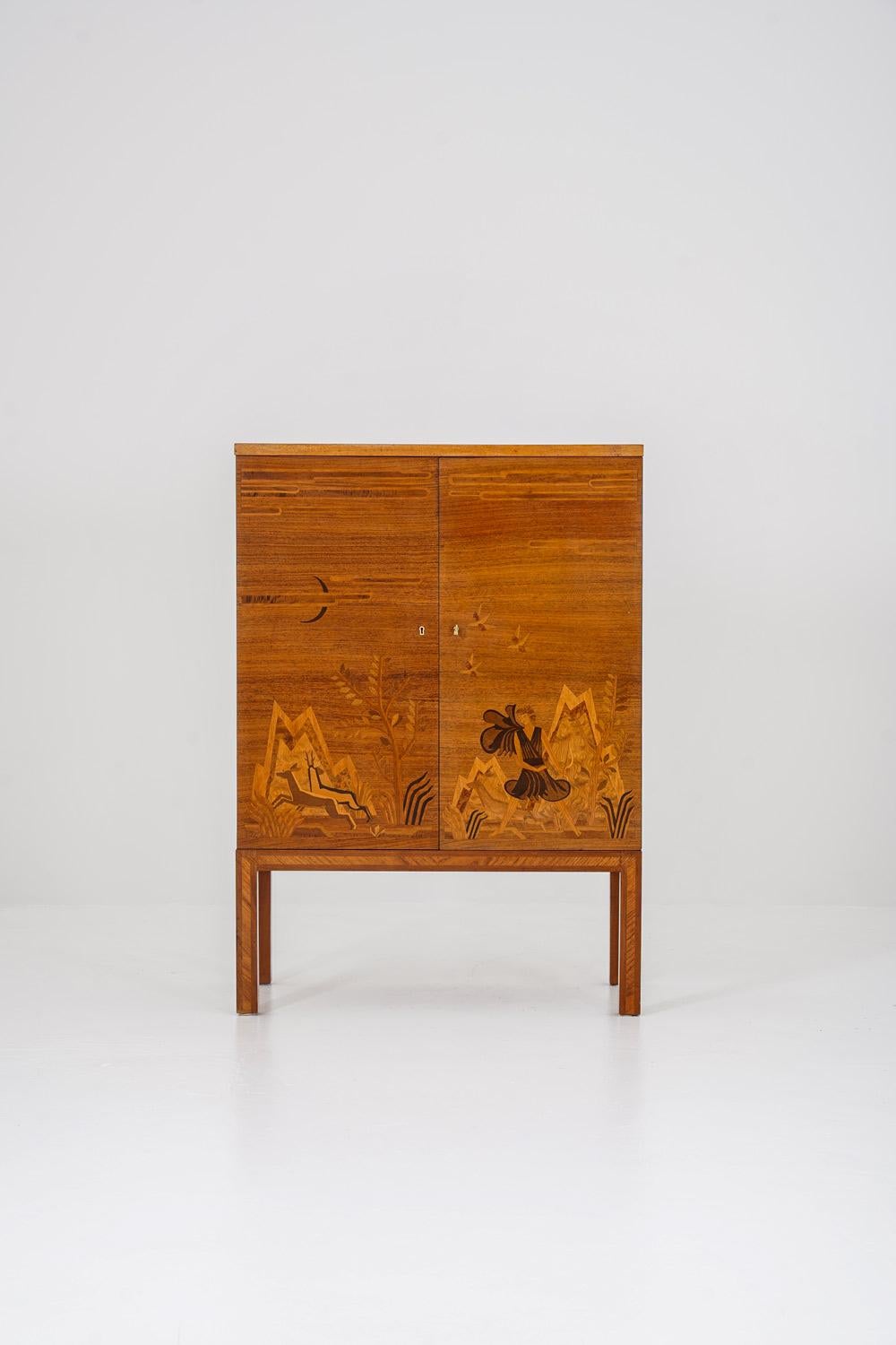 Elegant bar cabinet from the 1930s, showcasing the elegant craftsmanship characteristic of Swedish Modern design. Crafted in rich golden elm veneer with exquisite marquetry depicting a stylized landscape scene, featuring mountains, flora, and a