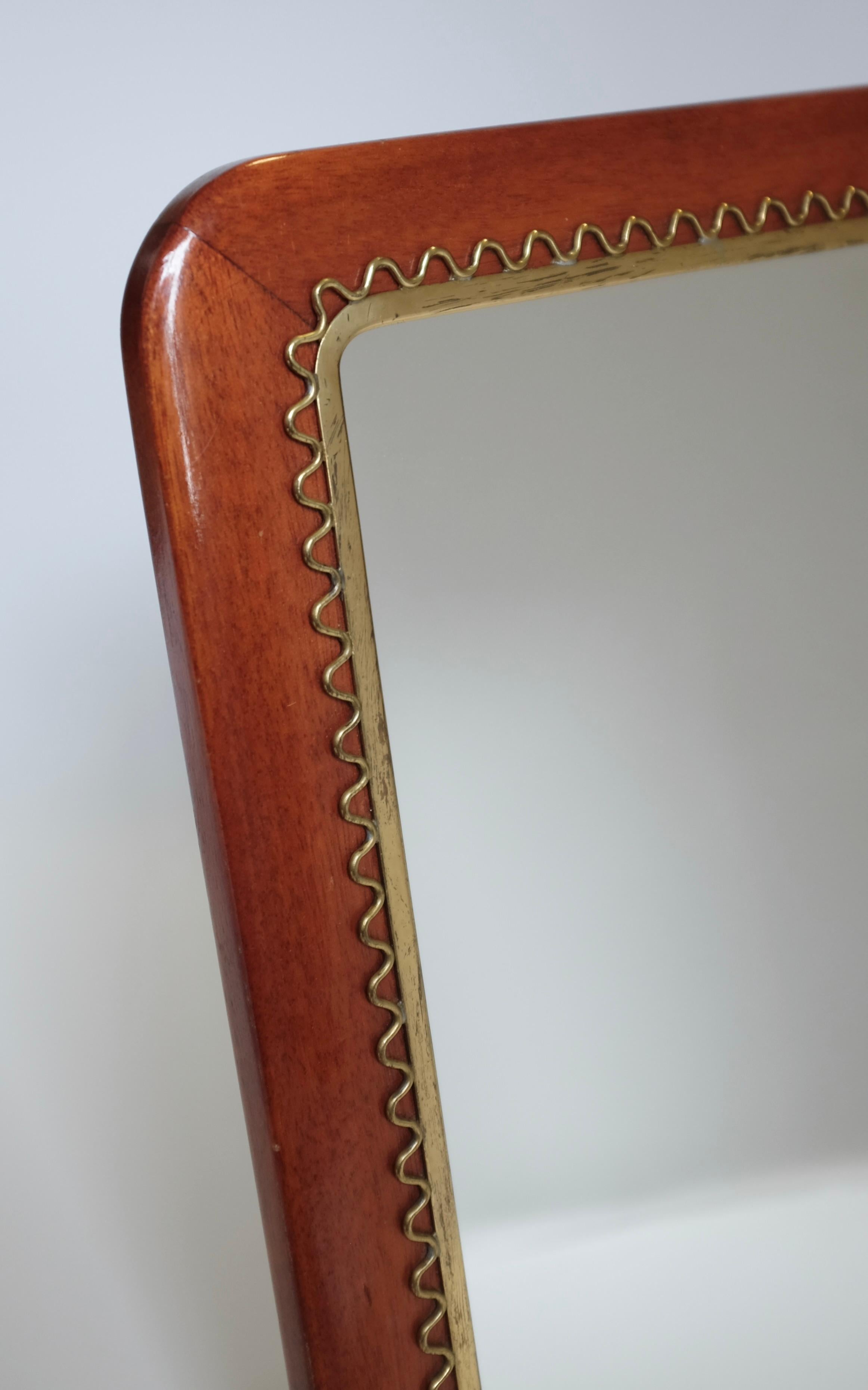 Magnifique miroir moderne suédois en laiton et acajou dans le style de Josef Frank et Svenskt Tenn. Des détails filigranes entourent le verre en laiton avec un cadre en acajou de forme rectangulaire. Peut être utilisé aussi bien comme miroir de