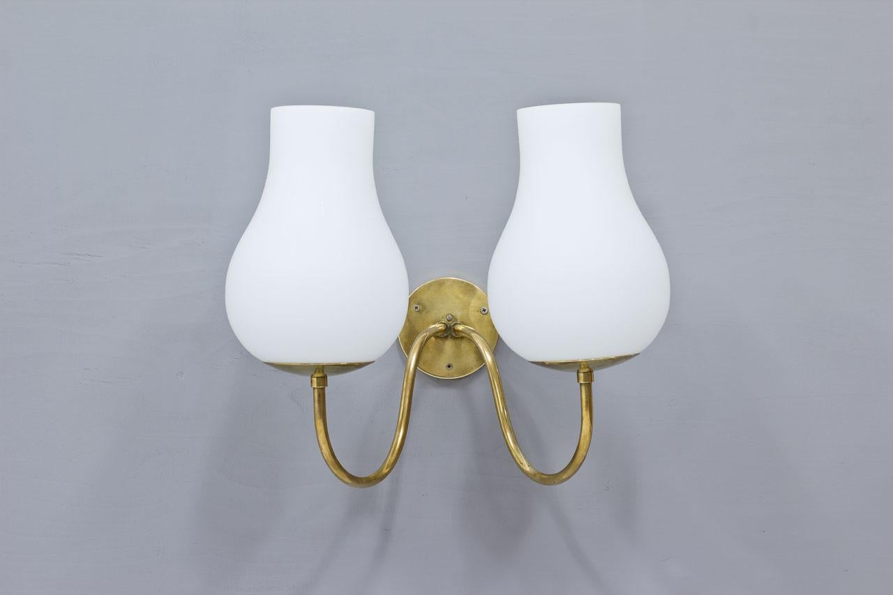 Elegant and large wall lamp manufactured in Sweden during the 1940s. 
Unattributed to any designer or maker. 
Made from brass with two large white opaline glass diffuser. 
The lamp is in very good vintage condition with patina and minor signs of