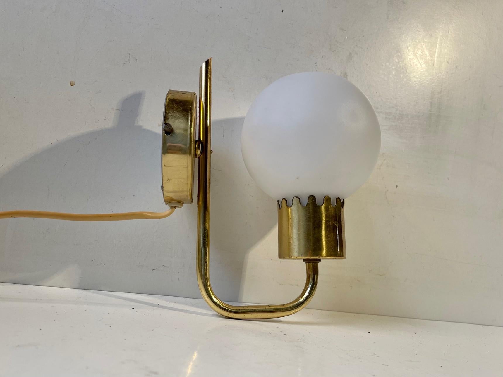A Paavo Tynell or Hans Agne Jakobsson inspired wall light. Its composed of solid brass and features a round shade in cased opaline glass. Designed and manufactured by Nya öia in Sweden during the 1960s. Measurements: Height 20, dept: 17, Shade