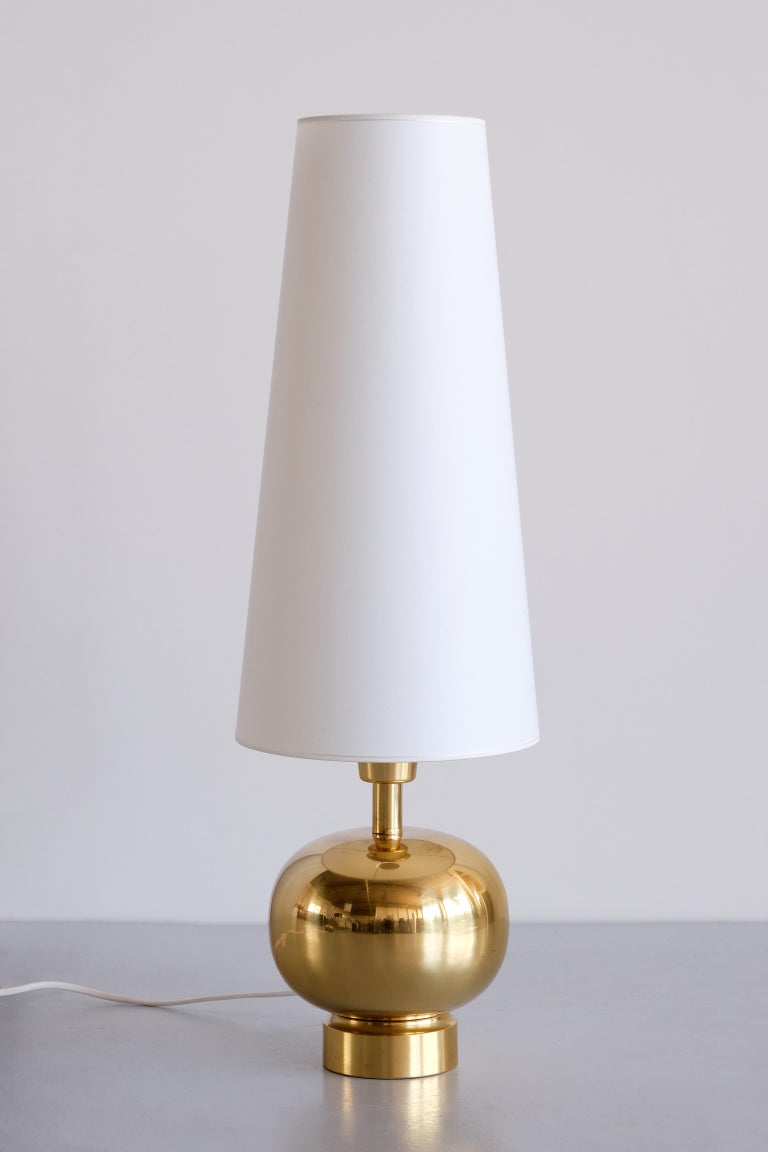 This striking table was lamp was produced by the Swedish manufacturer Aneta in the town of Växjö in the 1970s. The elegant sphere shaped base is made of polished brass. The tall, cone shaped shade has been renewed in an ivory color and offers a