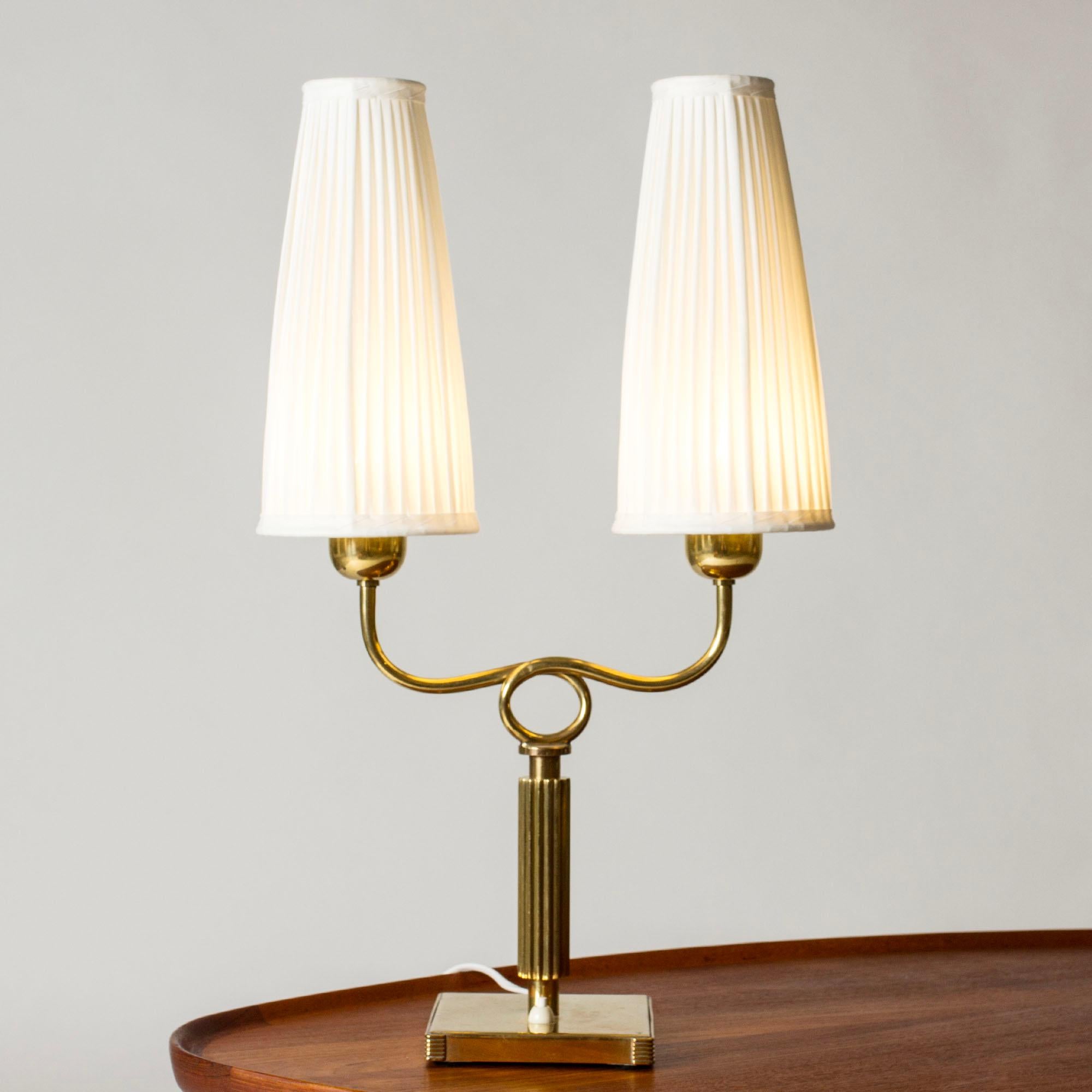 Elegant modernist brass table lamp, with a square base and embossed stripes. Decorative loop detail. Tall, pleated shades.