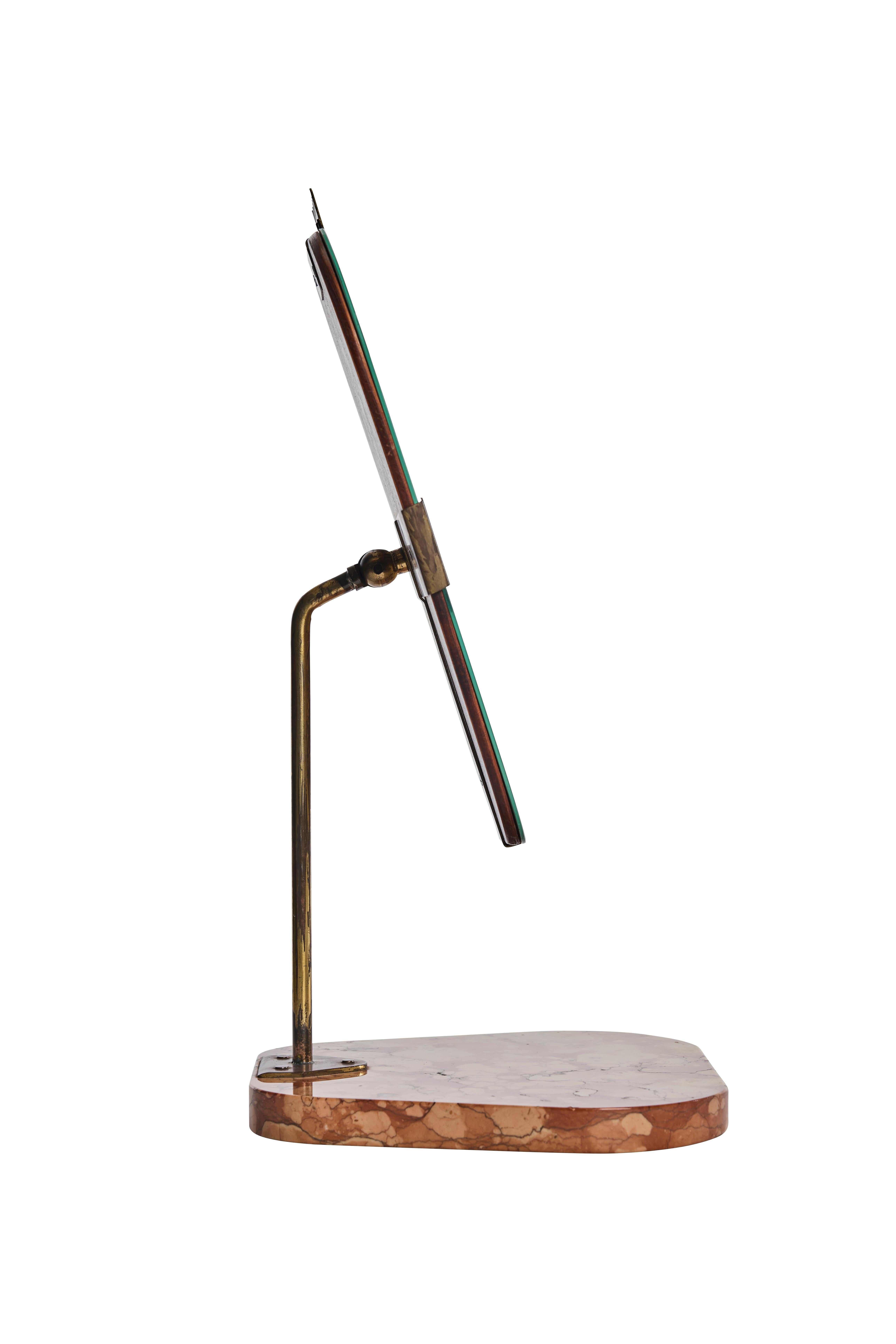 Elegant and sculptural, this Swedish Modern table mirror from the 1940s features a sleek brass frame set on a beautifully shaped marble base. The mirror is held by stylized brass clips with decorative cutouts, allowing the angle to be adjusted for