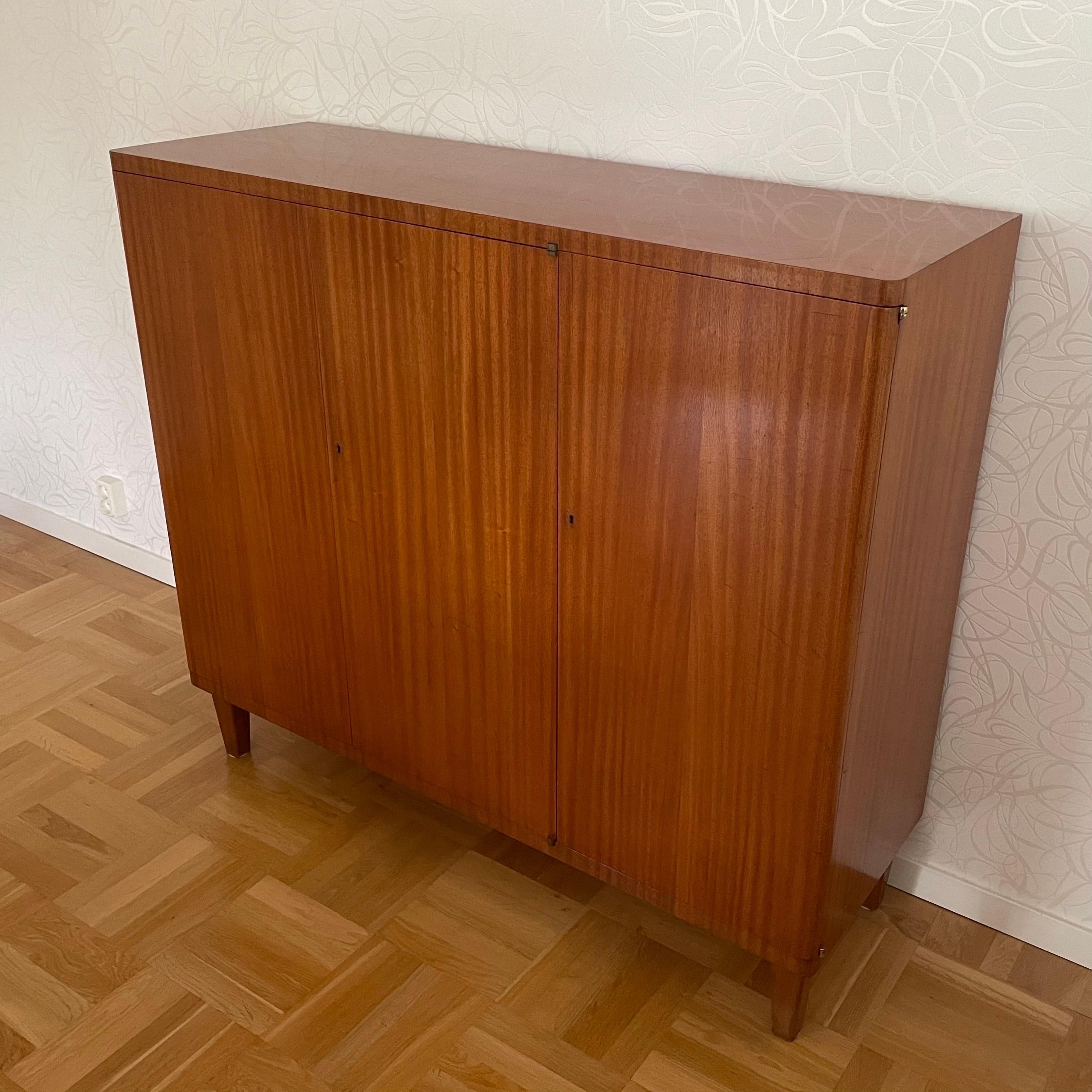 This is a Swedish Modern three doors cabinet manufactured by Nordiska Kompaniet 1944. The designed is attributed to Axel Einar Hjorth.

It comes veneered in mahogany.
The inside and the shelves are veneered with natural colored birch.
Behind the