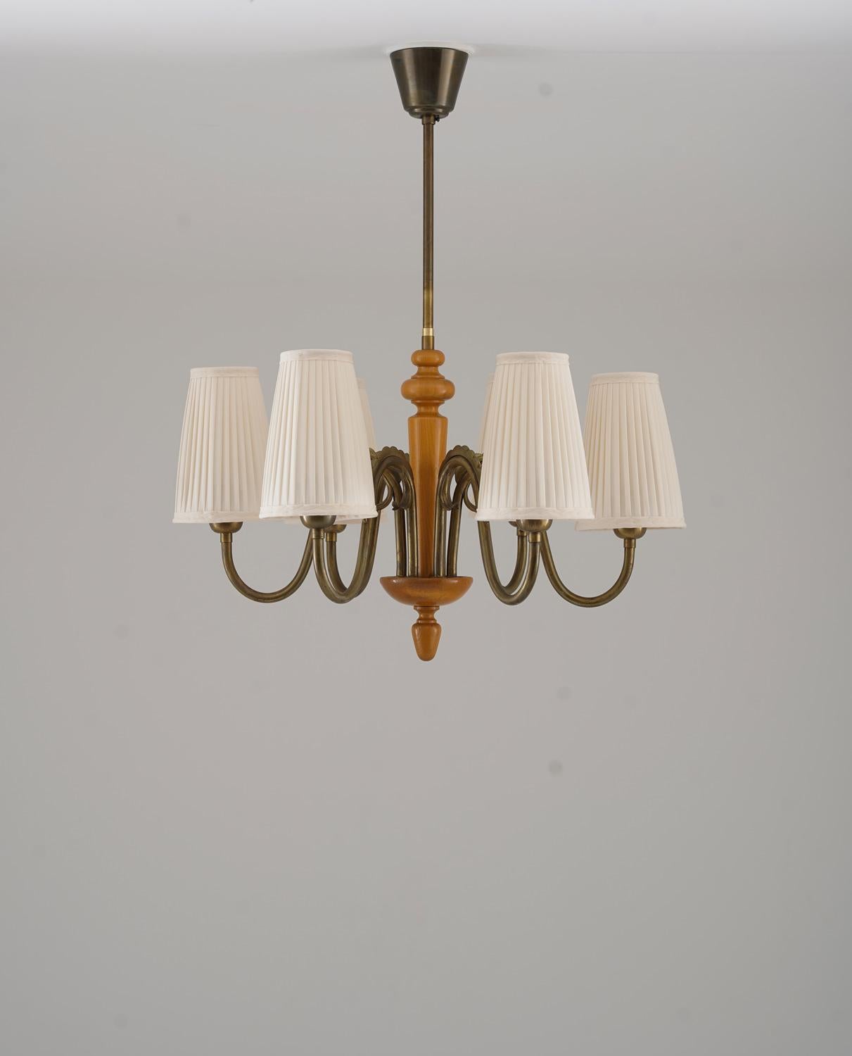 Elegant chandelier from the 1940s, crafted by Böhlmarks in Sweden. Executed in warm elm wood and patinated brass, this piece exemplifies the Swedish Modern style with its soft curves, refined proportions, and natural materials. The sculptural brass
