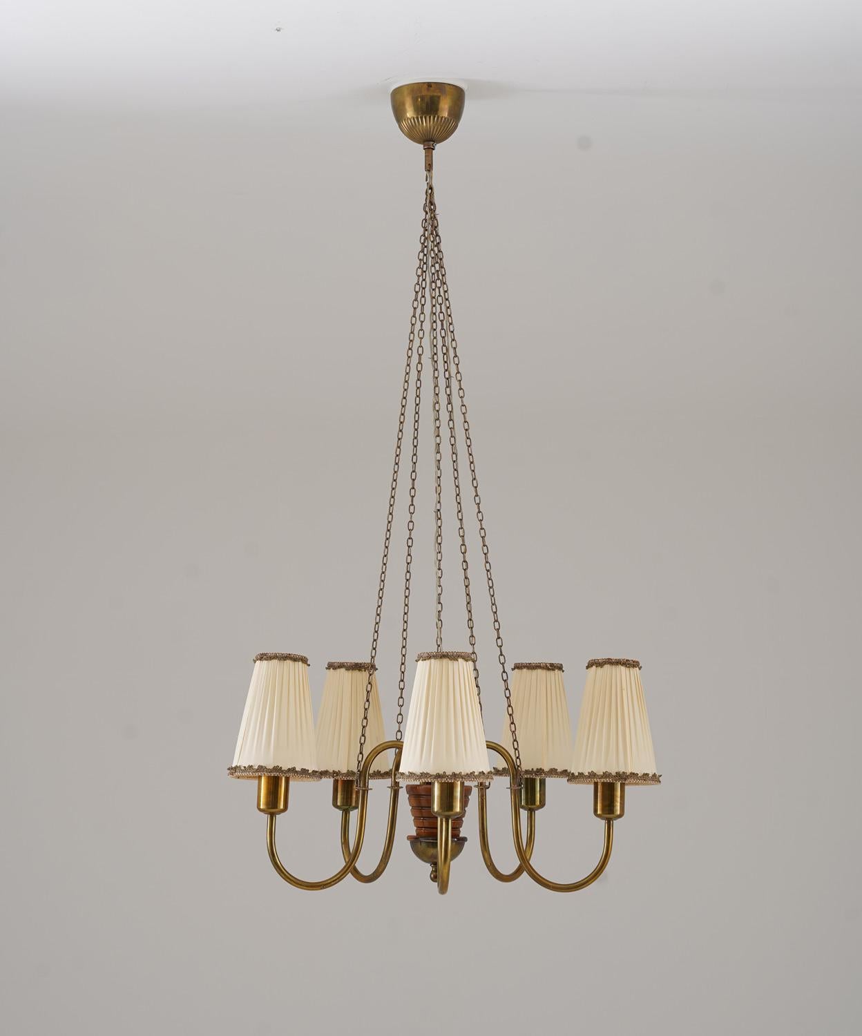 Very elegant Swedish Modern Chandelier, consisting of 5 light sources, supported by brass rods that are connected to a wooden center piece. Each light source is hidden by an original fabric shade. The lamp hangs from chains, connecting each arm to