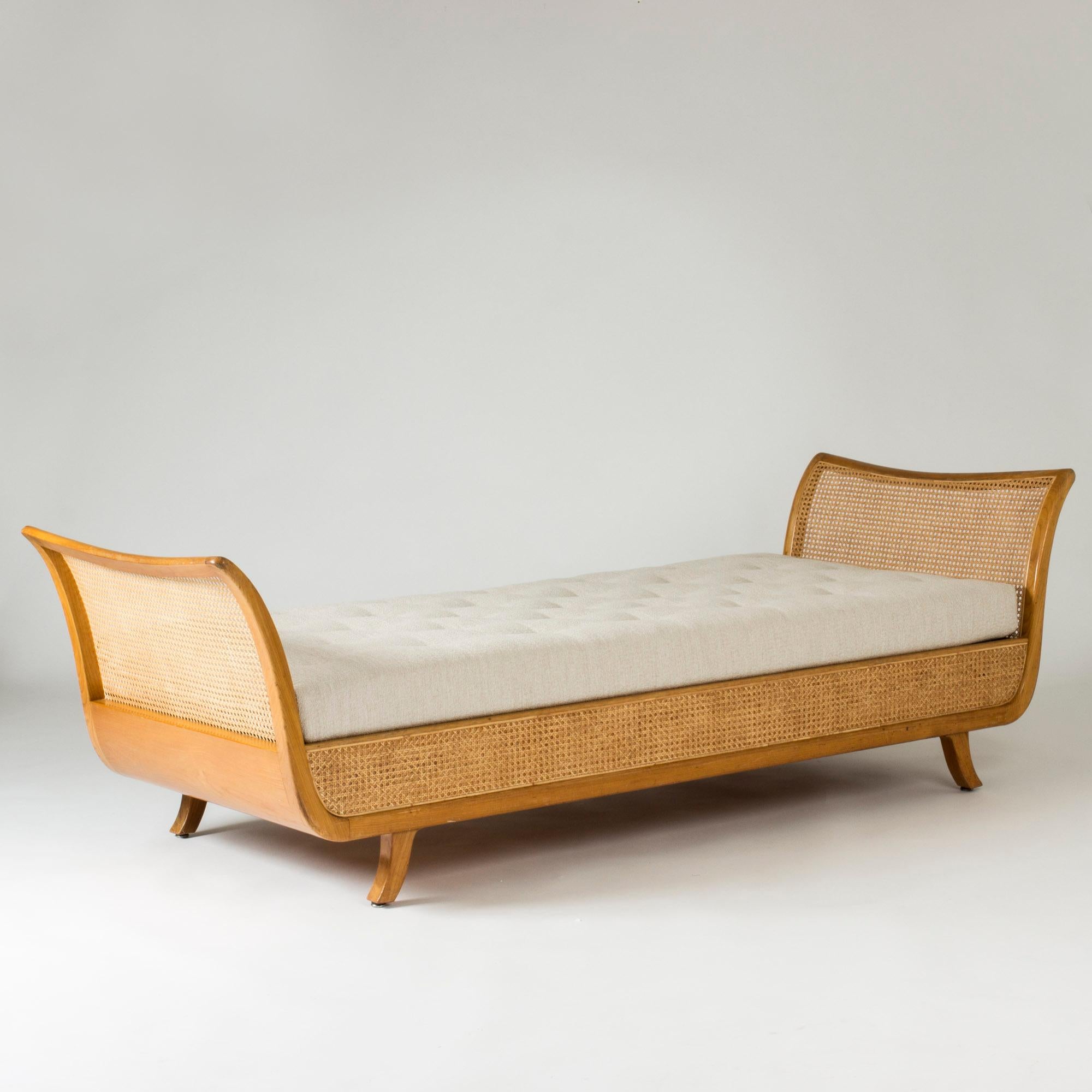 Beautiful Swedish Modern daybed, made from mahogany. Beautiful curved lines. Sides and ends dressed with rattan. Mattress upholstered with bouclé fabric, brown leather buttons. Hidden space underneath the mattress, which can be used for storage.