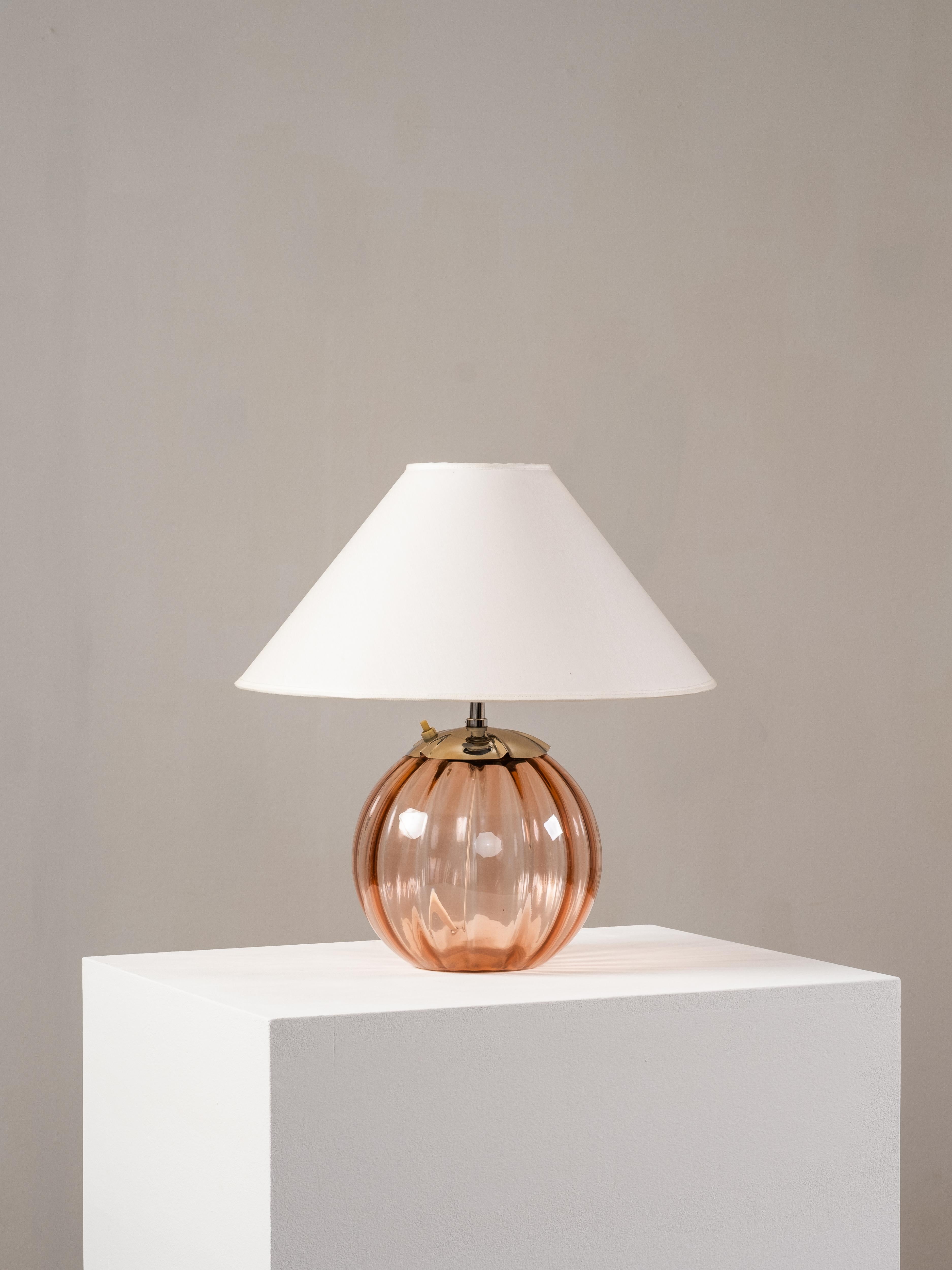 Lampe de table suédoise des années 1940 avec une base ronde en verre strié dans un ton rose poussiéreux. La lampe est finie avec un collier en laiton nickelé et associée à un abat-jour en tissu conique vintage, créant une lueur douce et