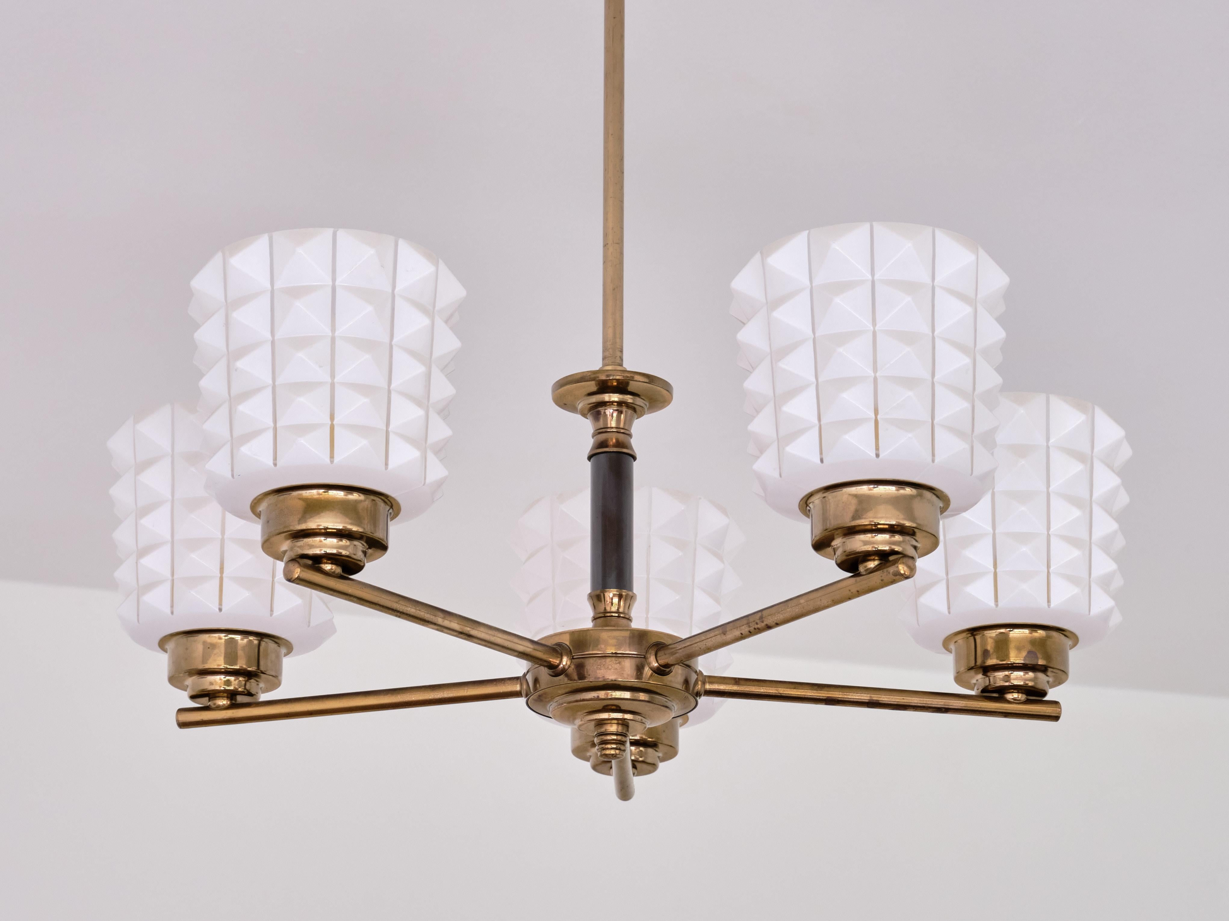 This striking chandelier was produced Sweden in the late 1950s. The fixture consists of a ceiling cup and central brass stem with the five brass arms attached to the lower centre. The distinct shades are made of a matte white opaline glass. The